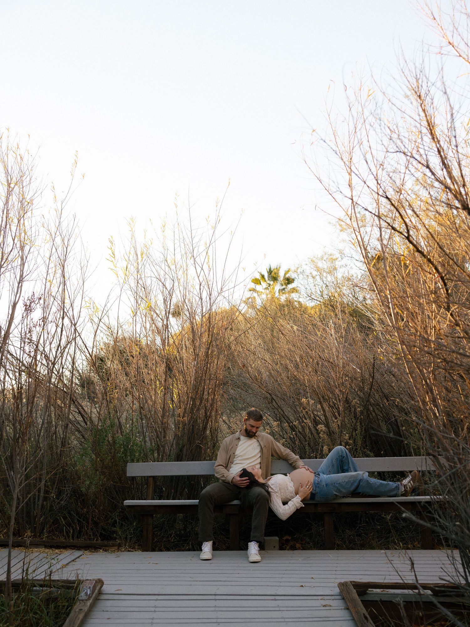 Couple relaxing on wooden deck surrounded by nature at sunset.