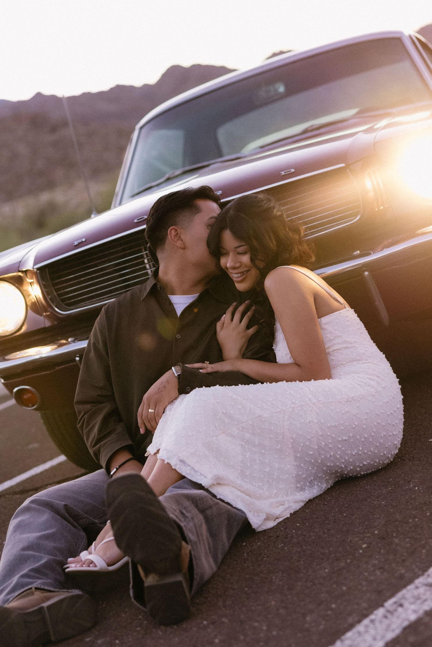 Couple lying beside vintage car during golden hour in desert setting.