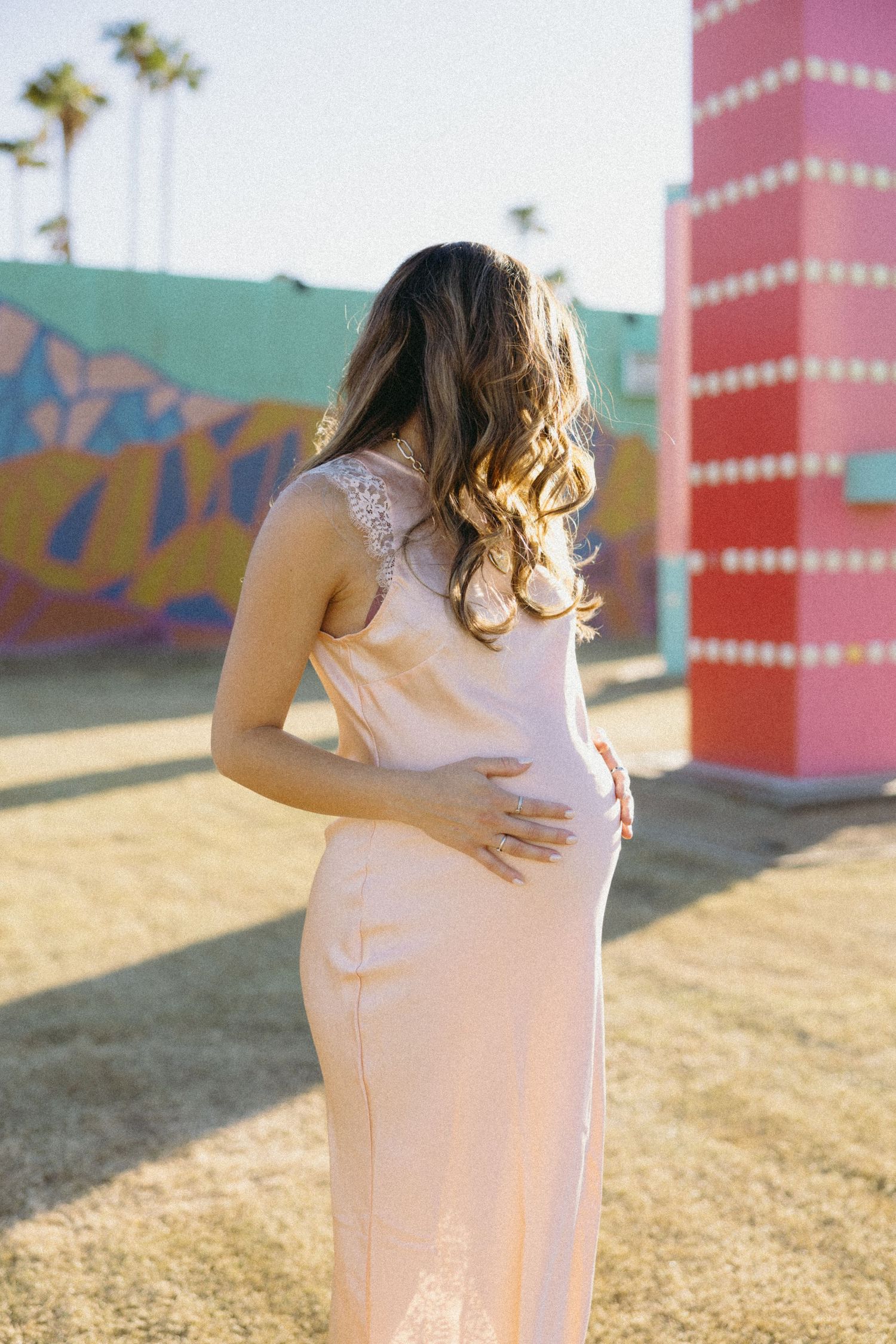 Maternity photos captured against vibrant pink and teal walls with artistic murals.