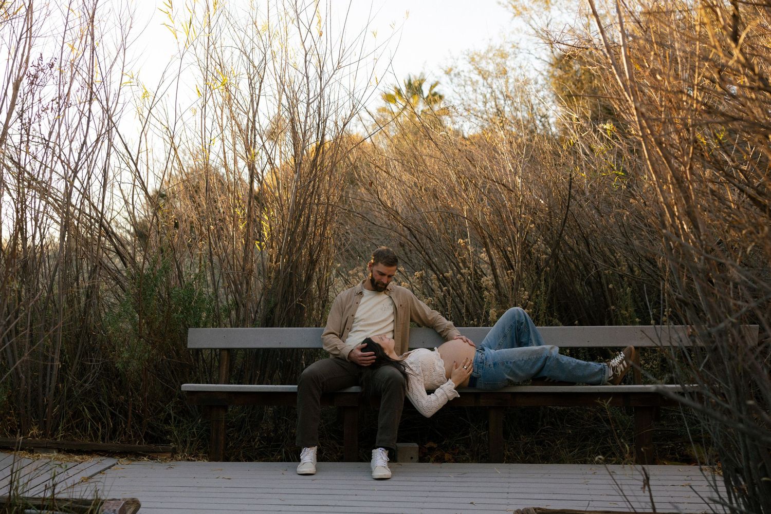 Couple relaxing on wooden bench surrounded by autumn foliage.