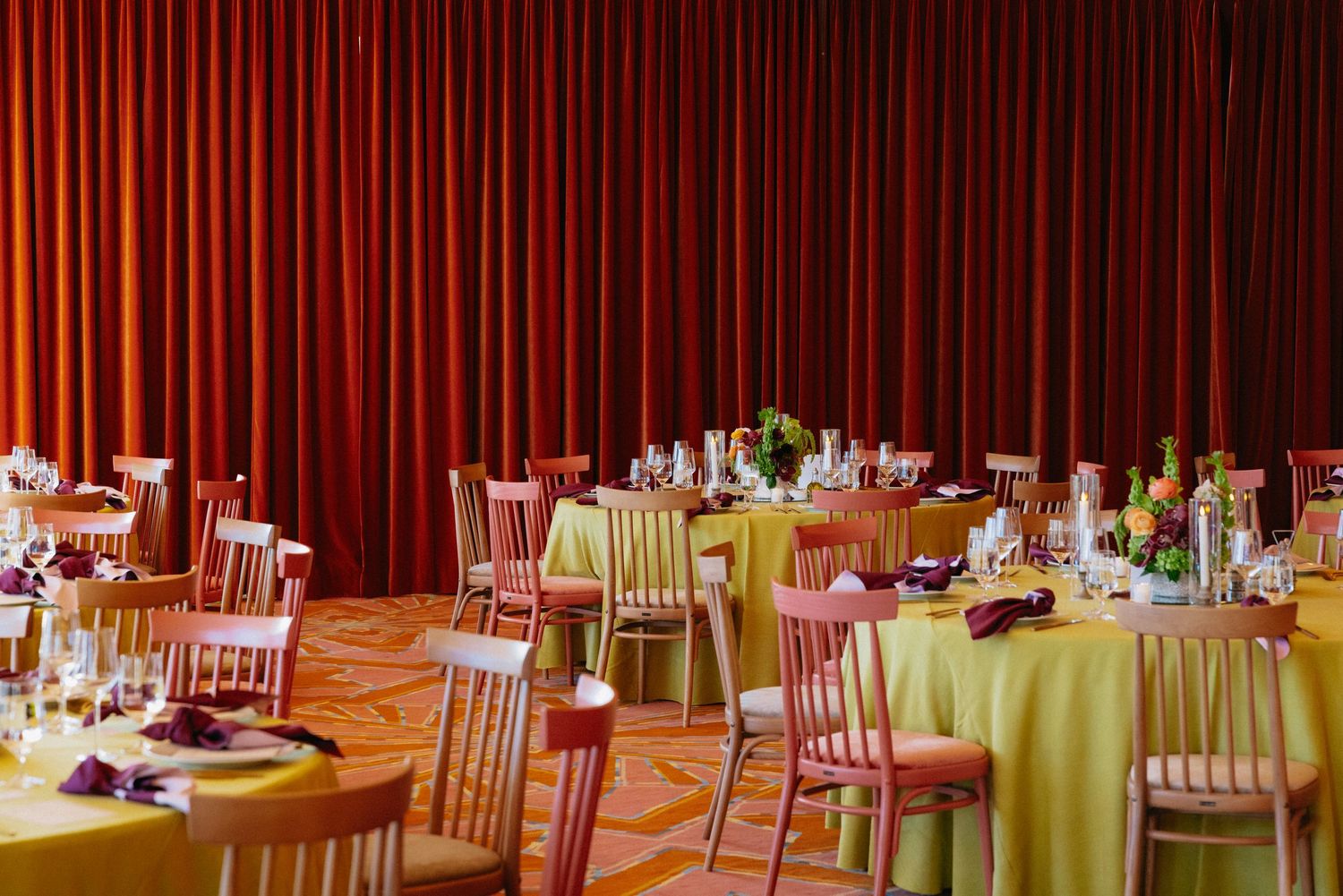 Elegant banquet hall with yellow tablecloths, red curtains, and chiavari chairs set for a formal event.