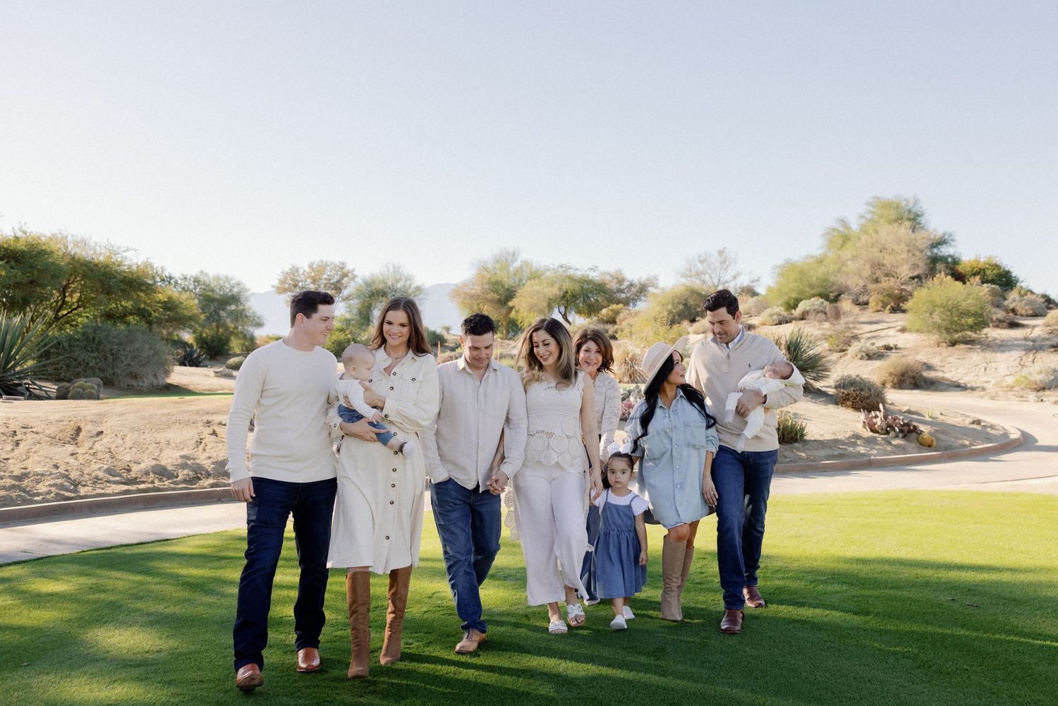 Extended family gathering outdoors on a grassy field with mountains in the background.