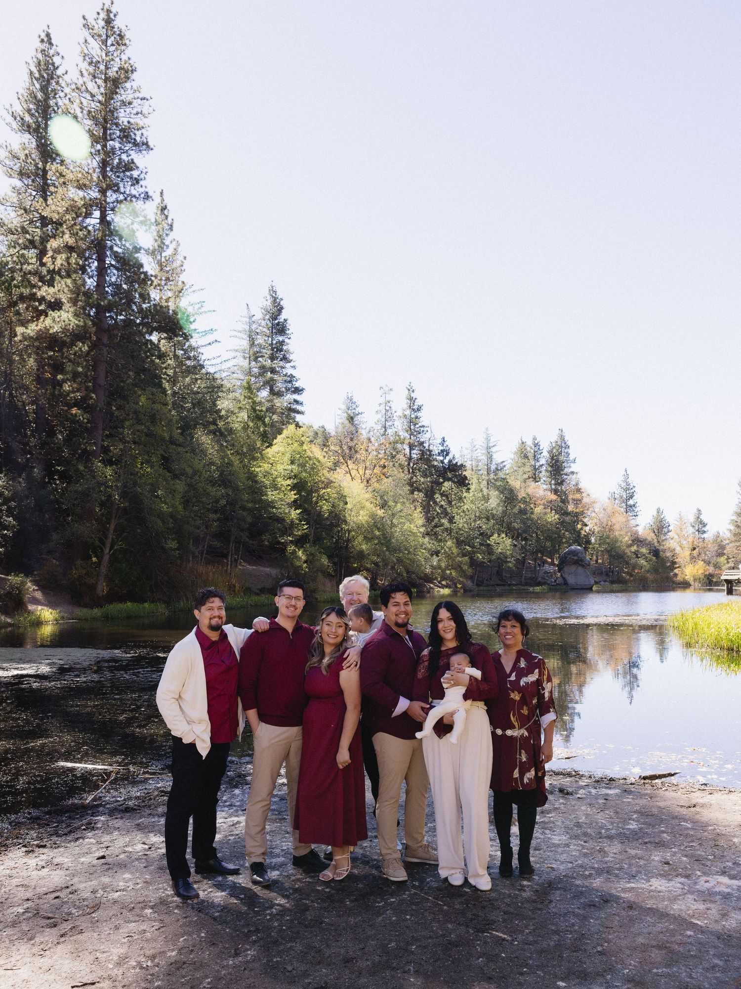 Extended family wearing coordinated burgundy and white outfits posed by a lakeside.
