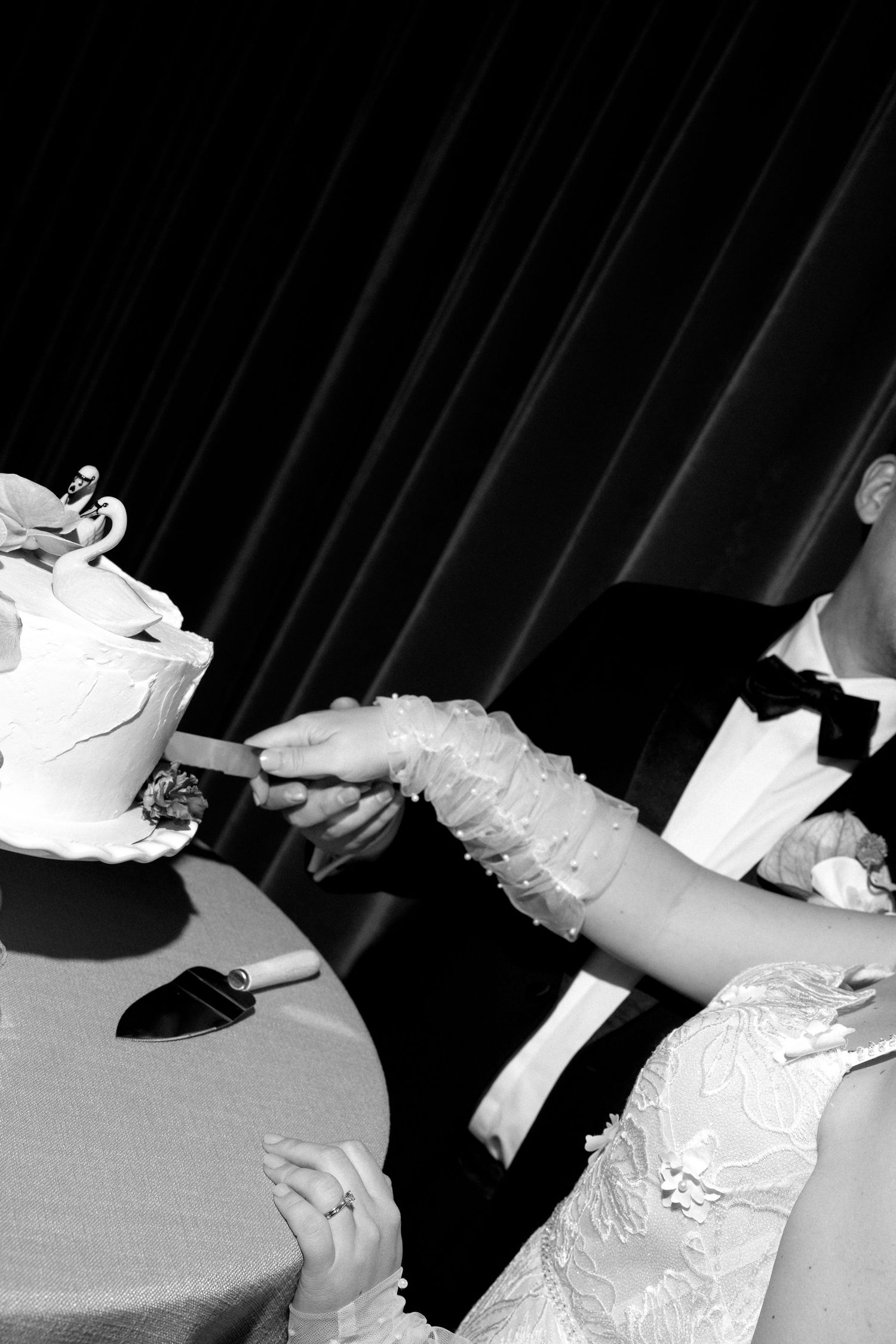 Black and white photo of bride and groom cutting their wedding cake together at reception.