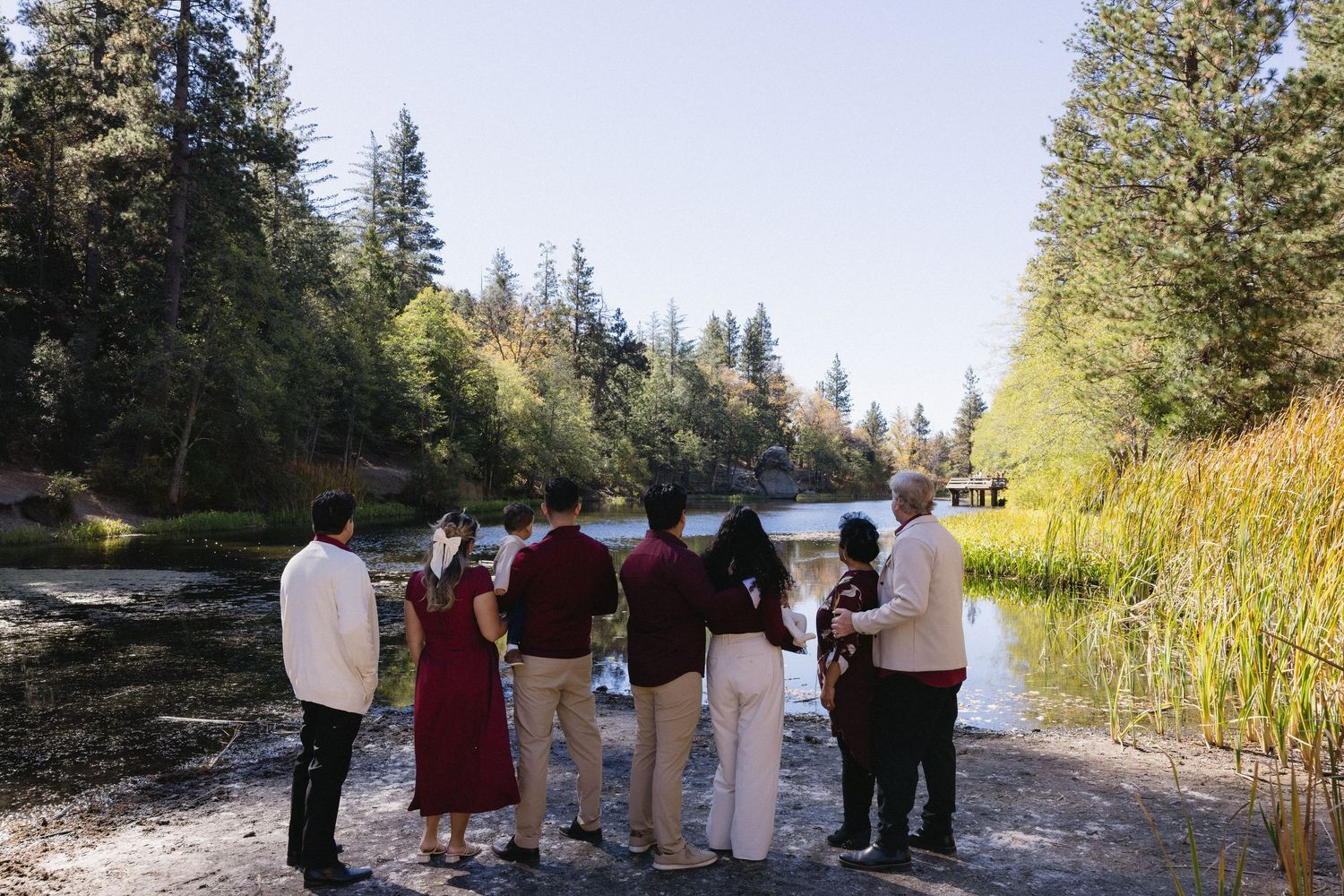 Family group portrait taken by a scenic lake with pine trees in the background.