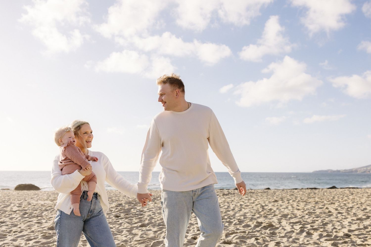 Family walking and playing together on a sunny beach with mountains in the distance.