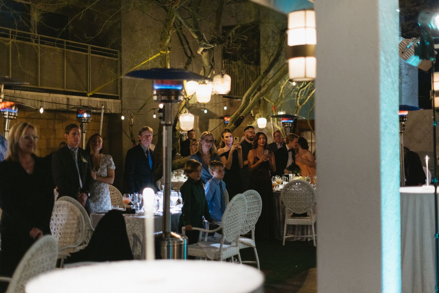 Guests mingling at an elegant indoor-outdoor evening event with warm ambient lighting and white furniture.