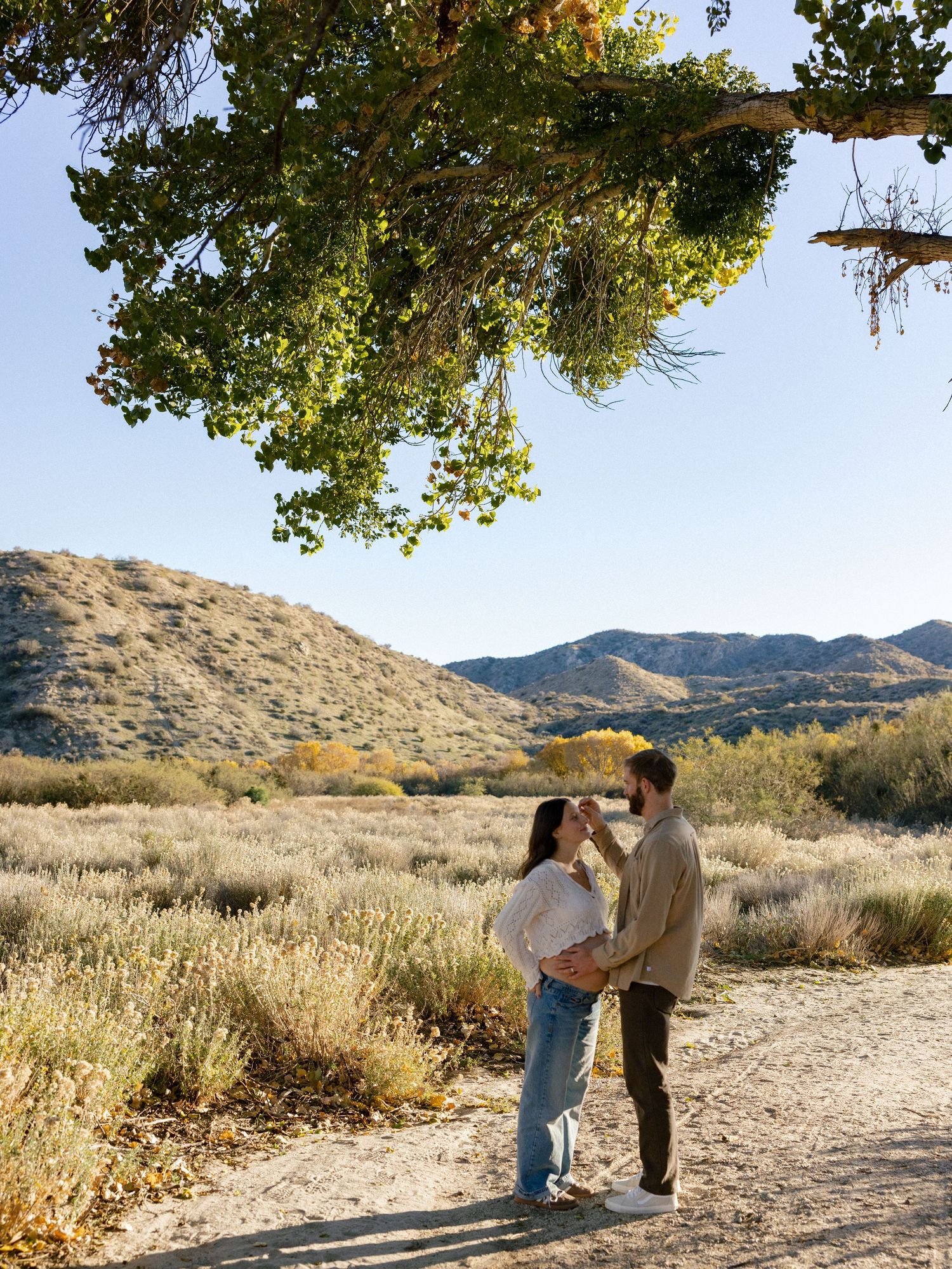 Couple walking along desert trail with mountains and autumn foliage in background.