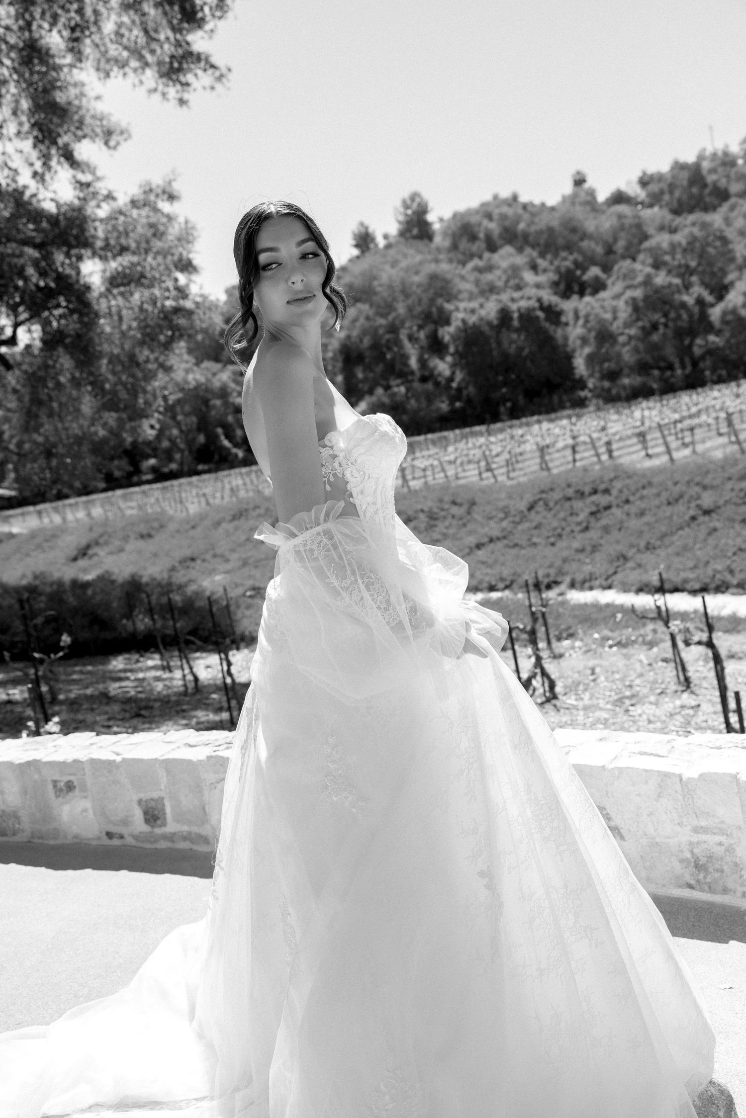 Elegant bride in a strapless ball gown poses gracefully outdoors in black and white portrait at vineyard wedding.