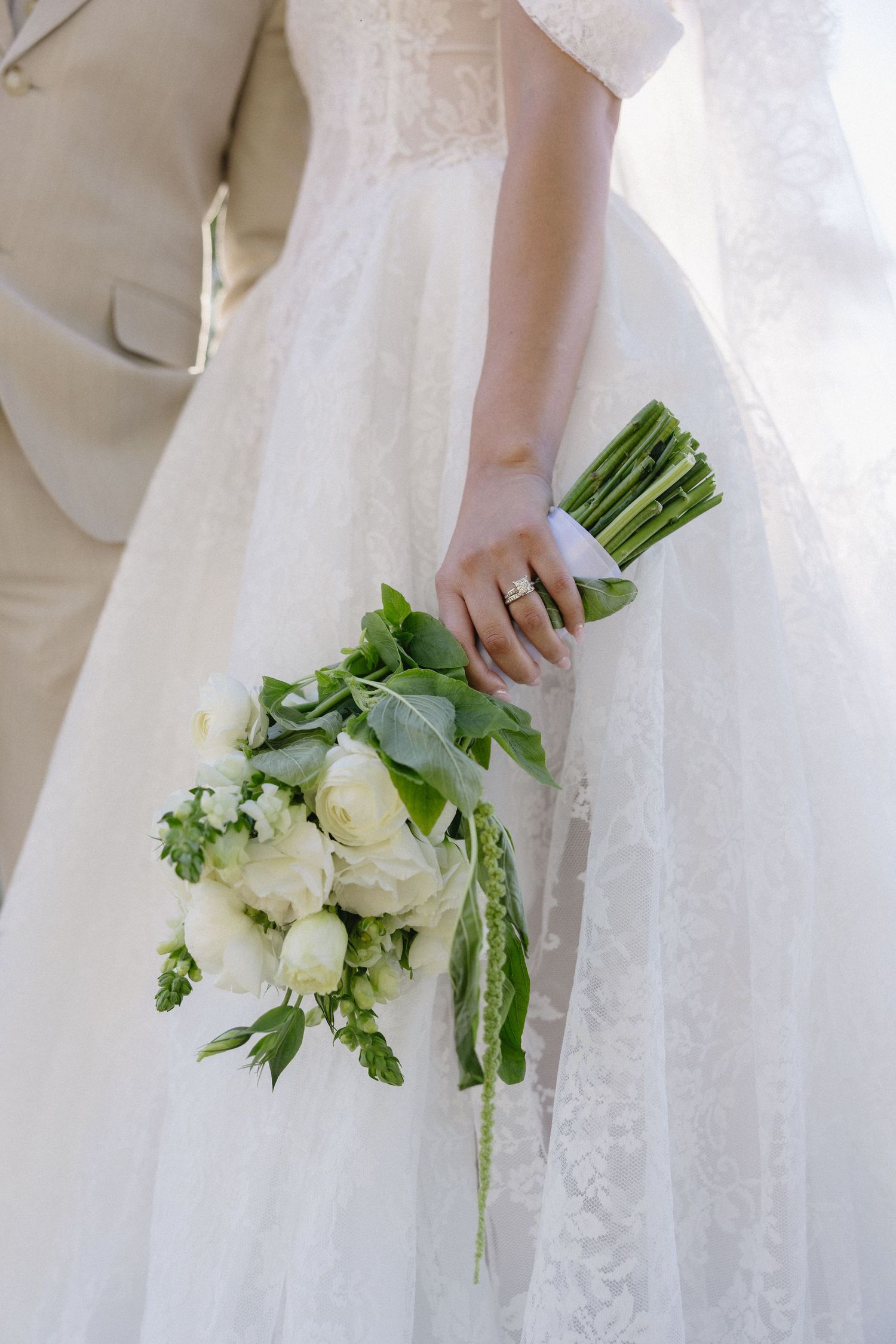A close-up of a white wedding bouquet with roses held against a flowing white dress.