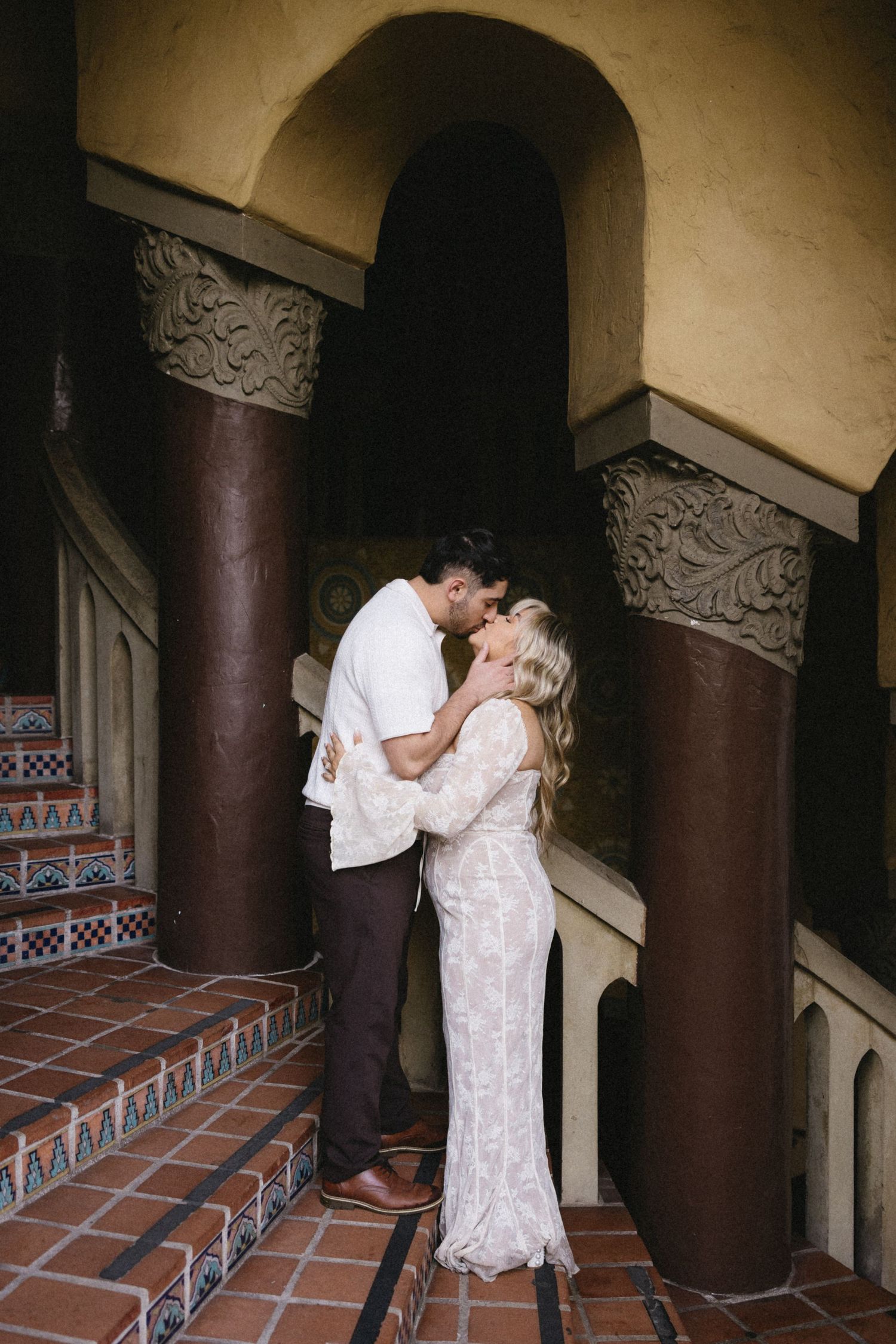 A couple embraces in an ornate Spanish colonial hallway with decorative tiles and columns.