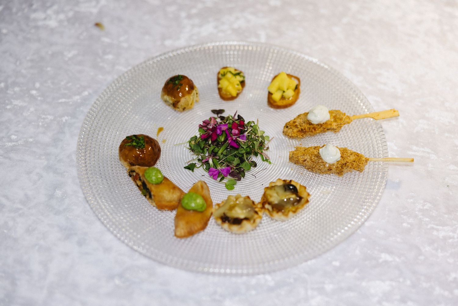 Elegant gourmet appetizer platter with assorted bite-sized hors d'oeuvres garnished with microgreens on a glass plate.