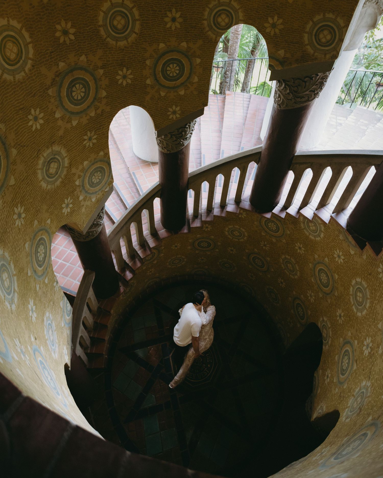 A spiral staircase with ornate wallpaper and dramatic lighting creates an artistic composition.