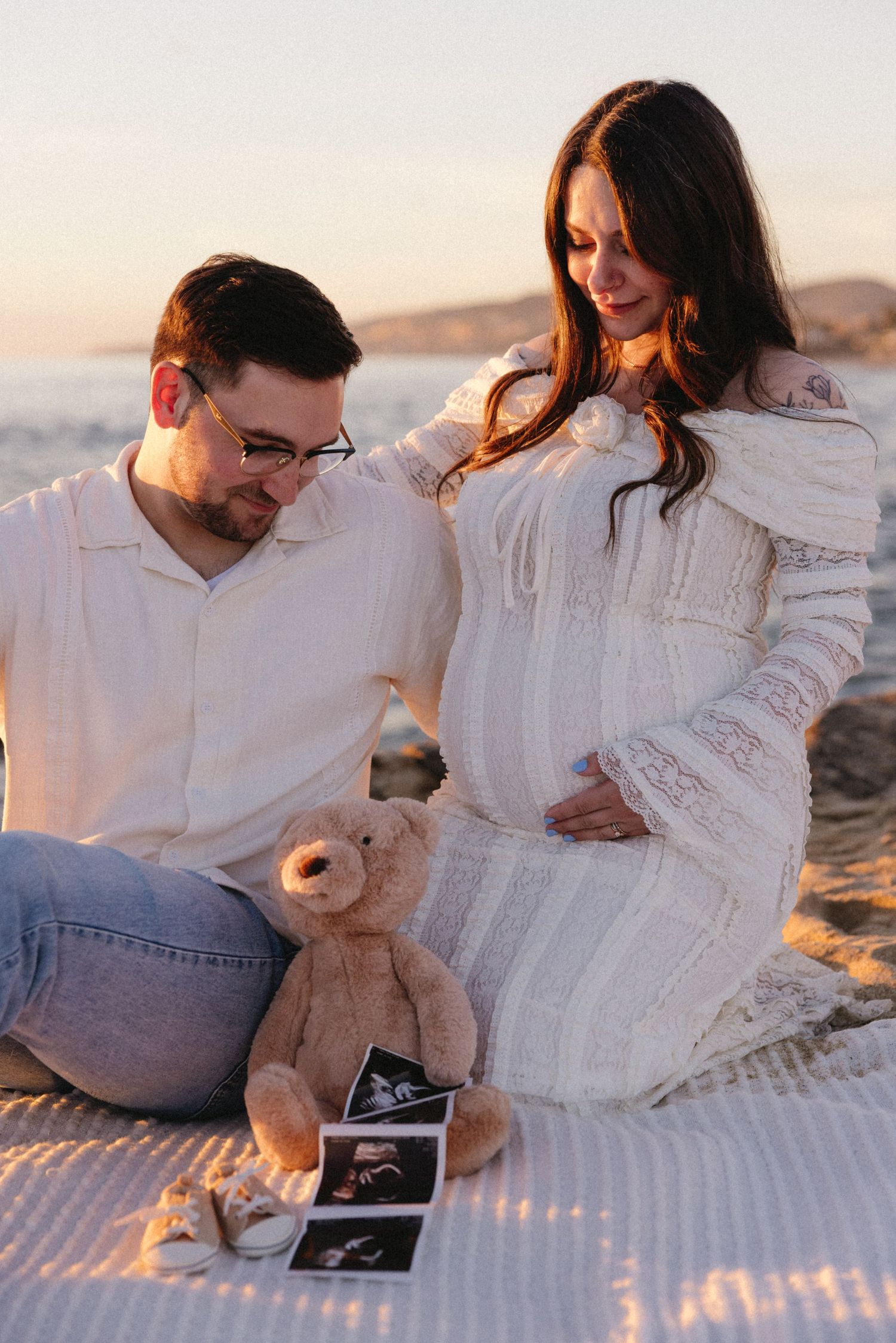 A couple looks at ultrasound photos while sitting on a blanket at the beach.