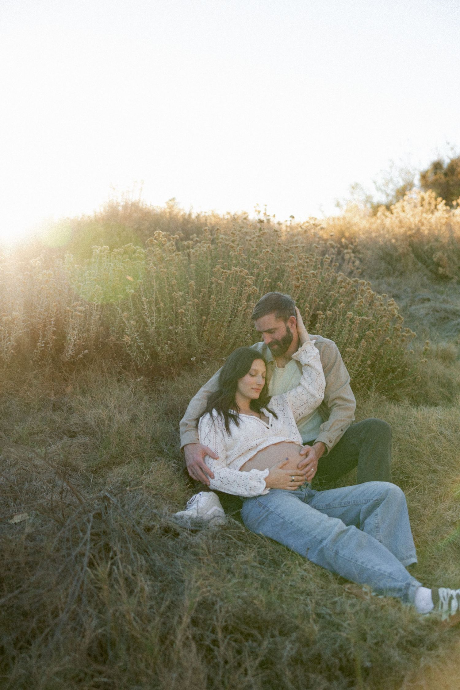 Couple lying together in tall grass during golden hour sunset.
