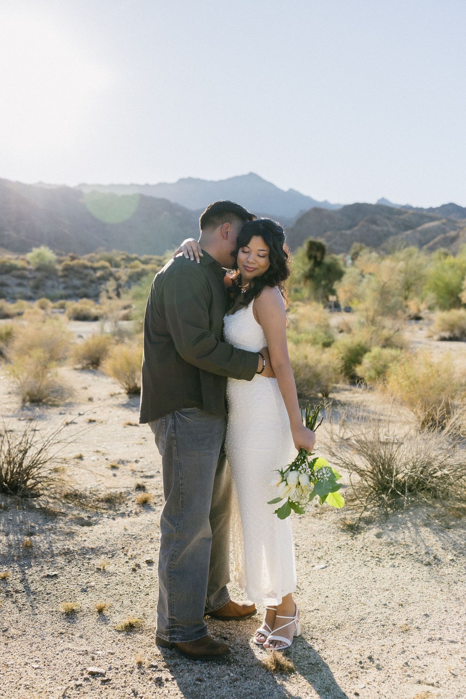 Romantic desert engagement photo shoot with couple embracing against mountain backdrop.