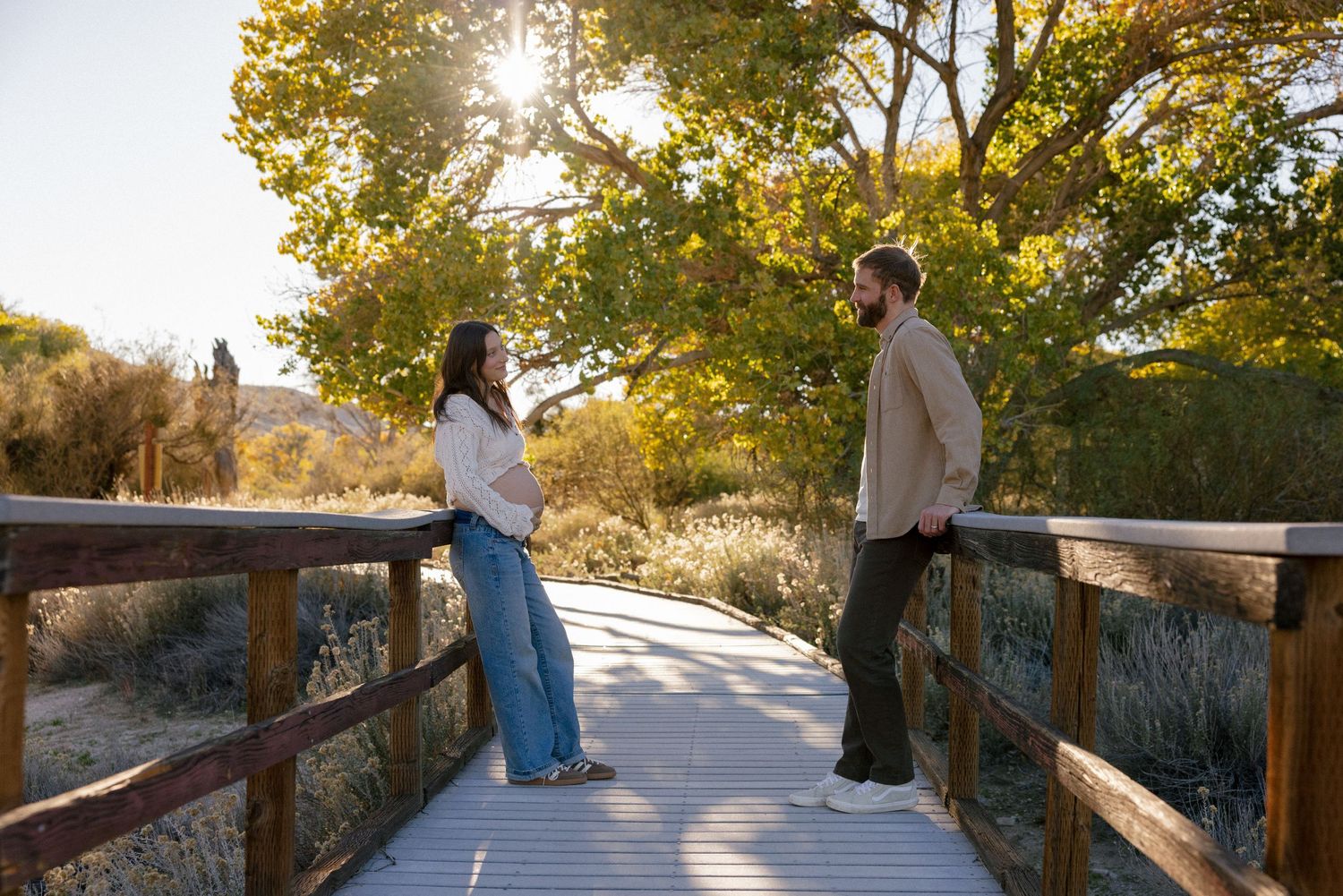 Golden sunlight streams through trees as couple walks along elevated wooden pathway.