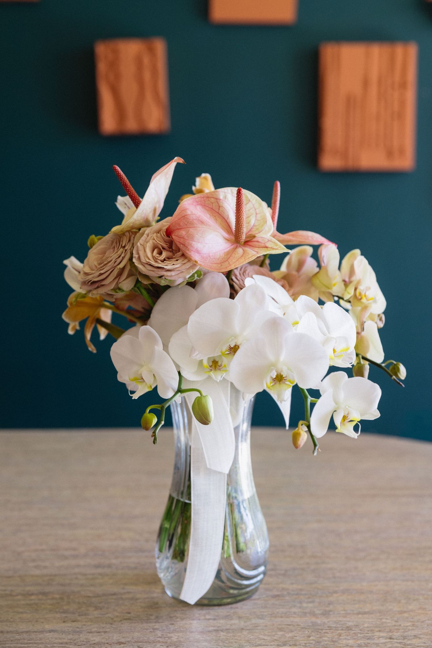 Wedding bouquet of white orchids, pink anthuriums, and roses in glass vase on table.