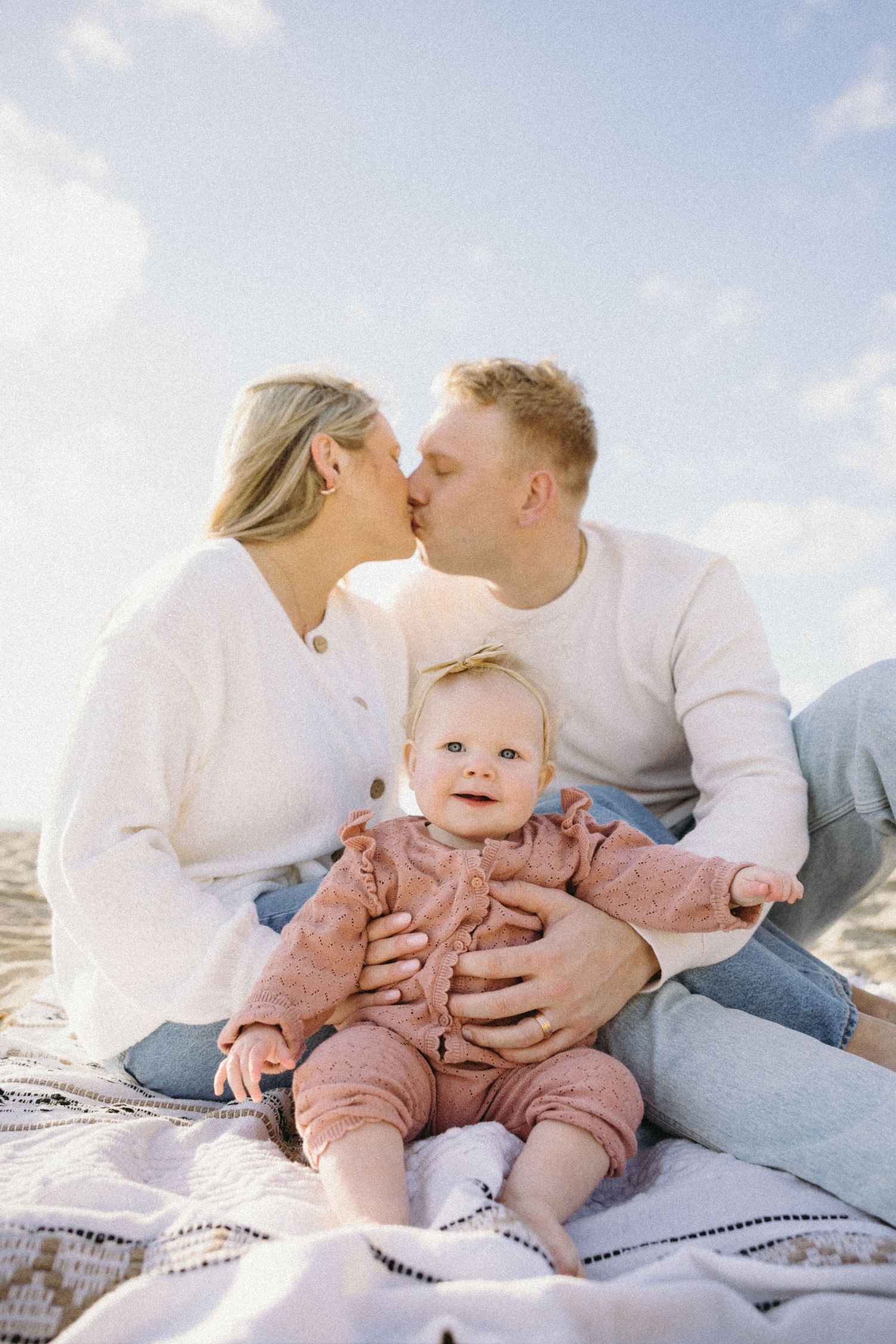 Family sharing tender moments on a blanket at the beach during a sunny day.