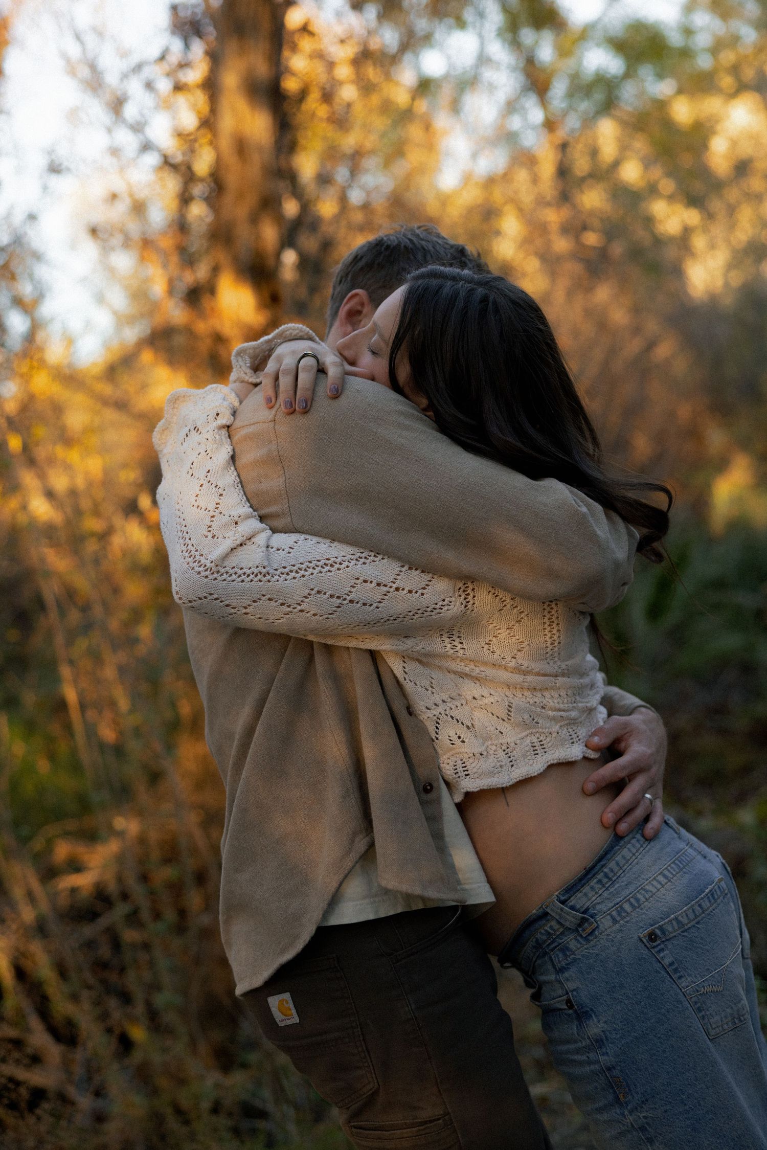 Intimate embrace captured in warm autumn sunlight among trees.