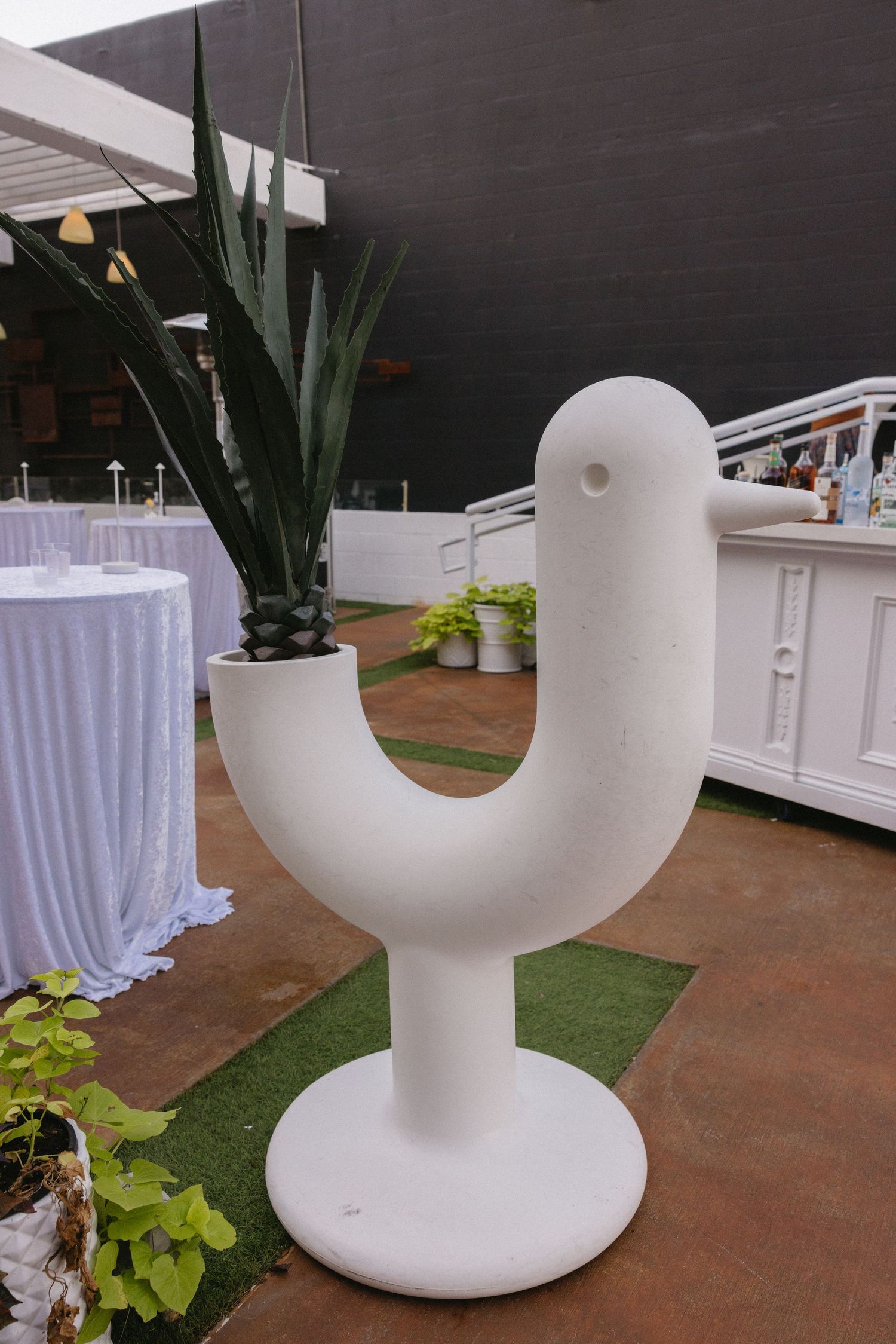 White sculptural bird-shaped planter holding a succulent plant on a patio near a bar area.