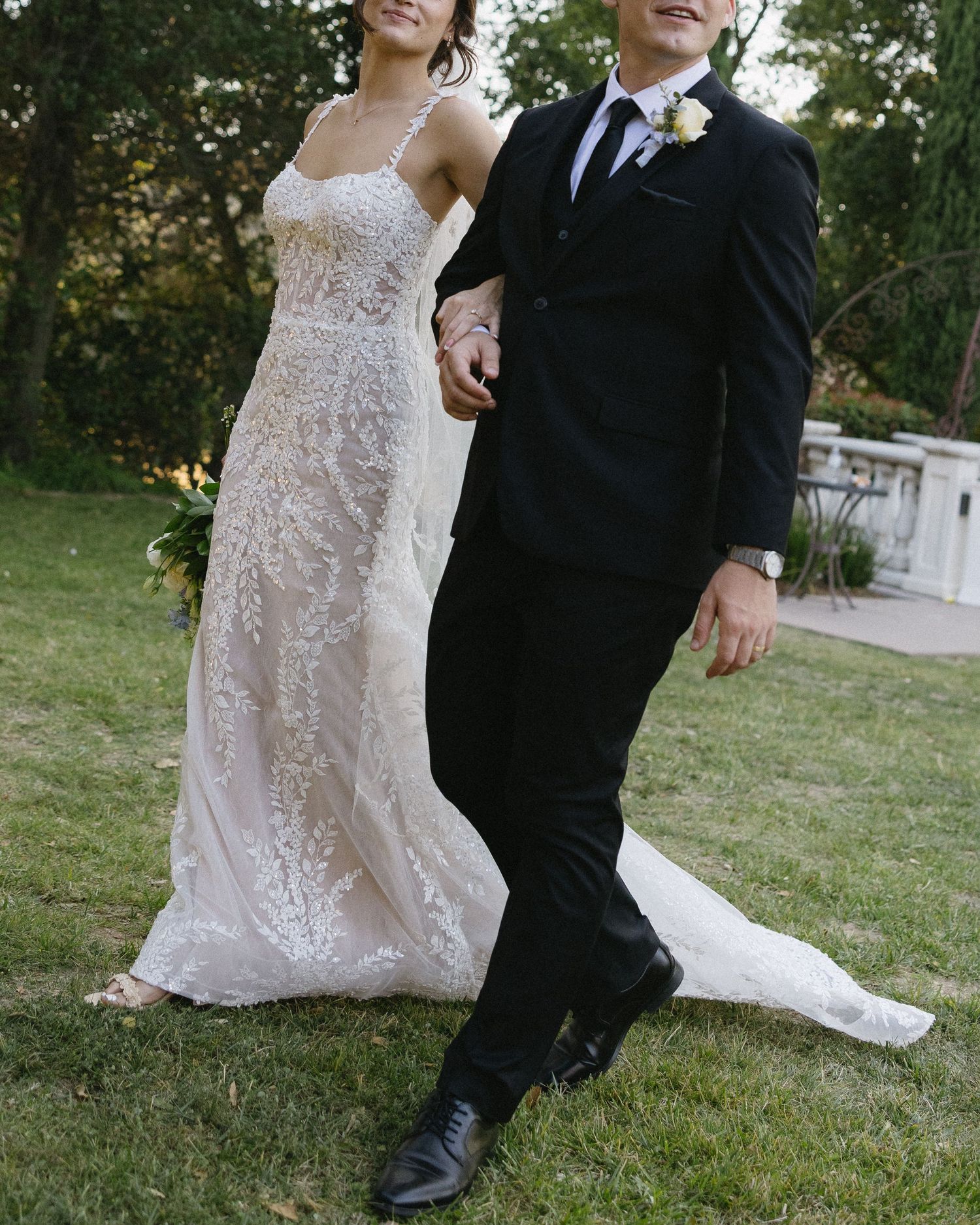 Candid wedding portrait of a couple walking together on grass in formal attire.