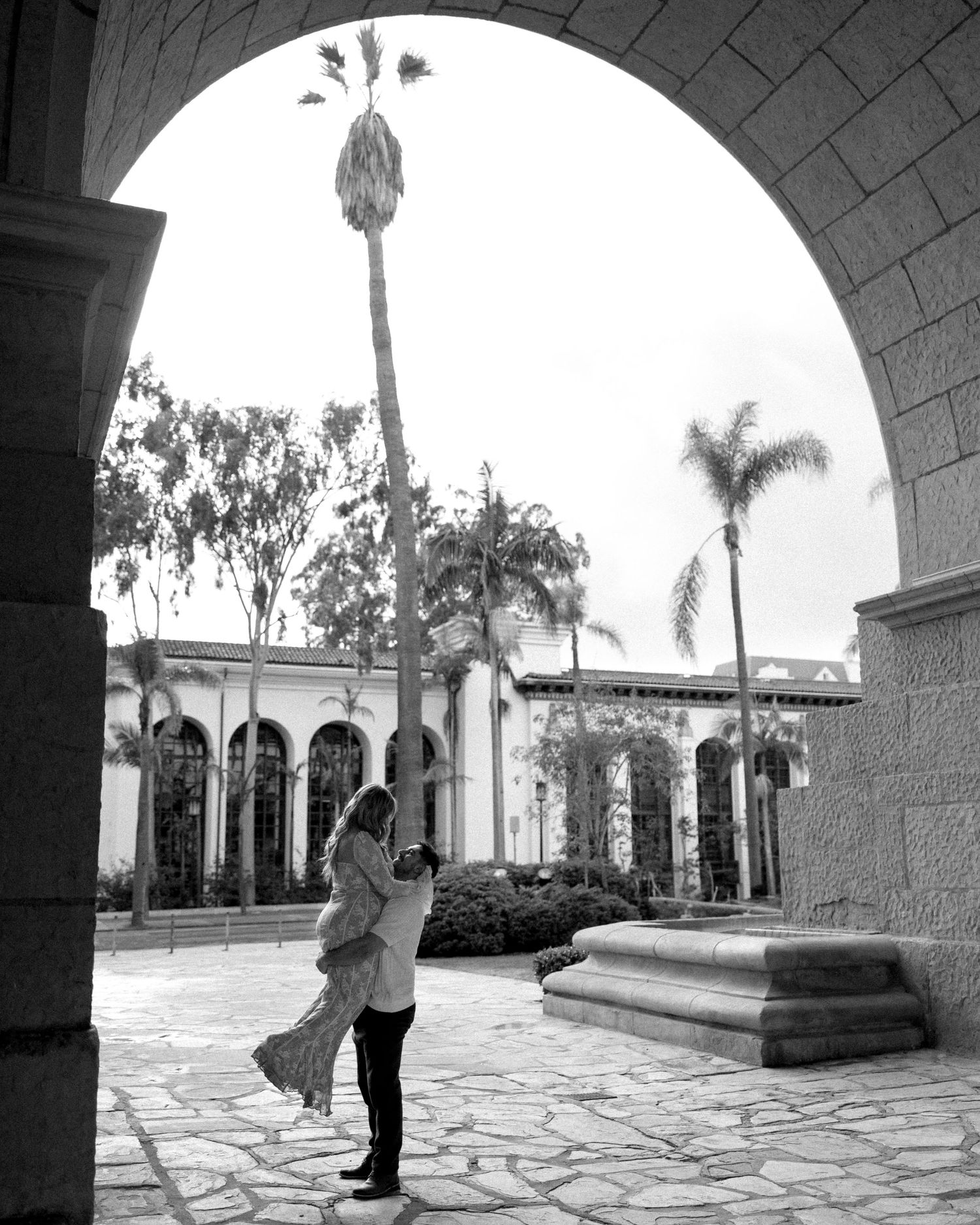 A romantic black and white photo sequence showing a couple in an elegant courtyard with arched architecture.