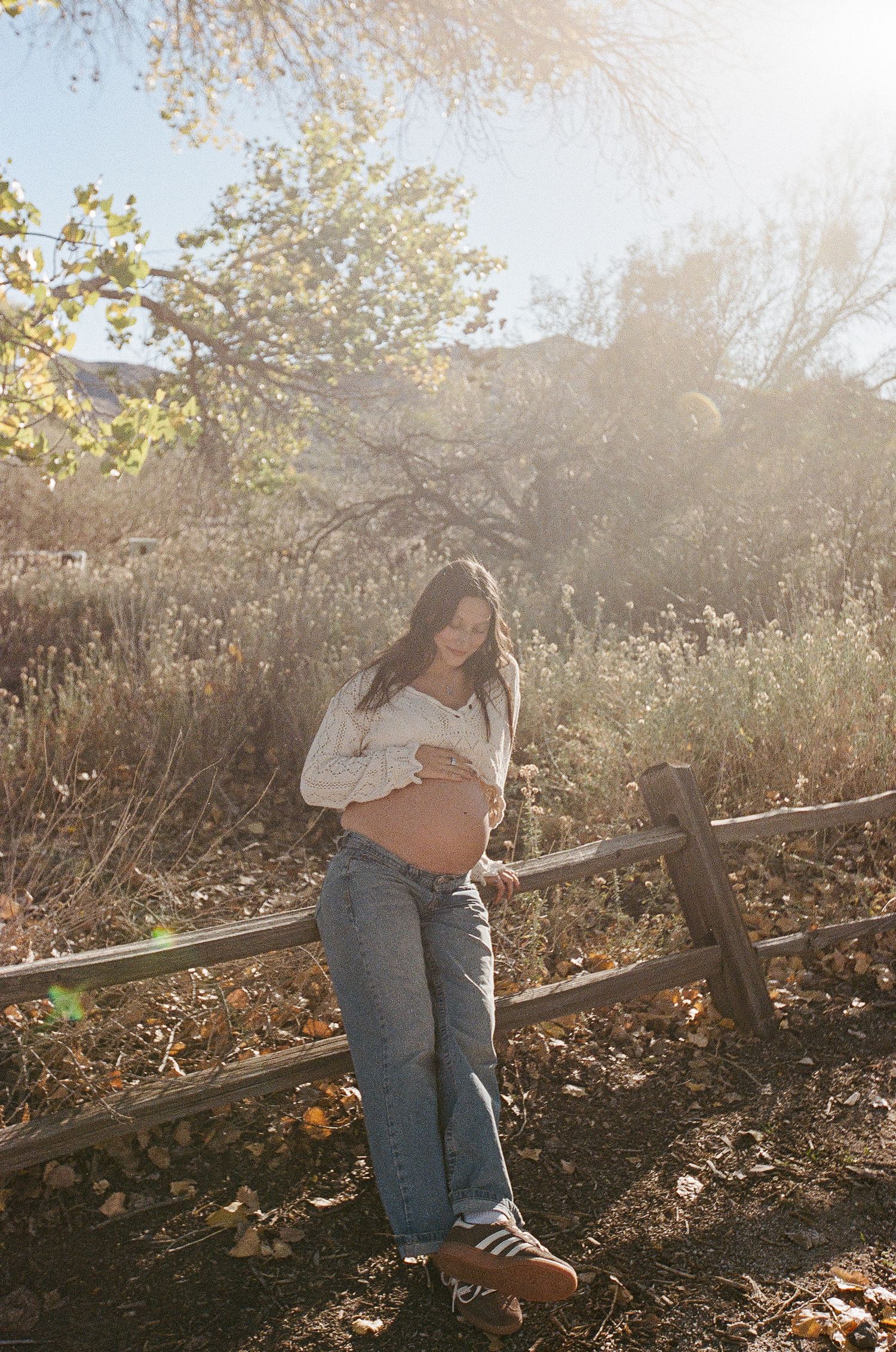 Person sitting on wooden fence in sunlit natural setting.