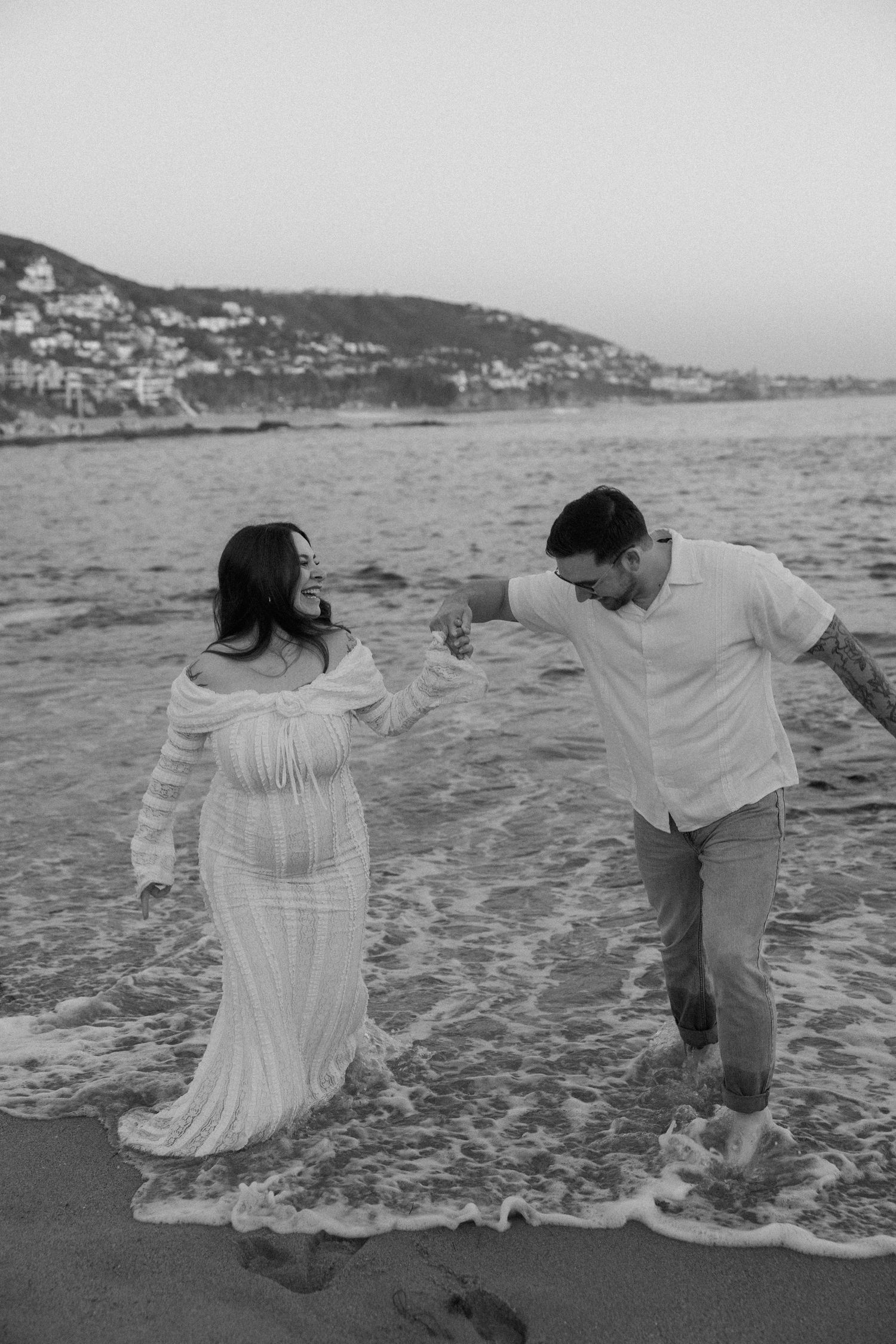 Playful couple dancing in ocean waves on beach at dusk.