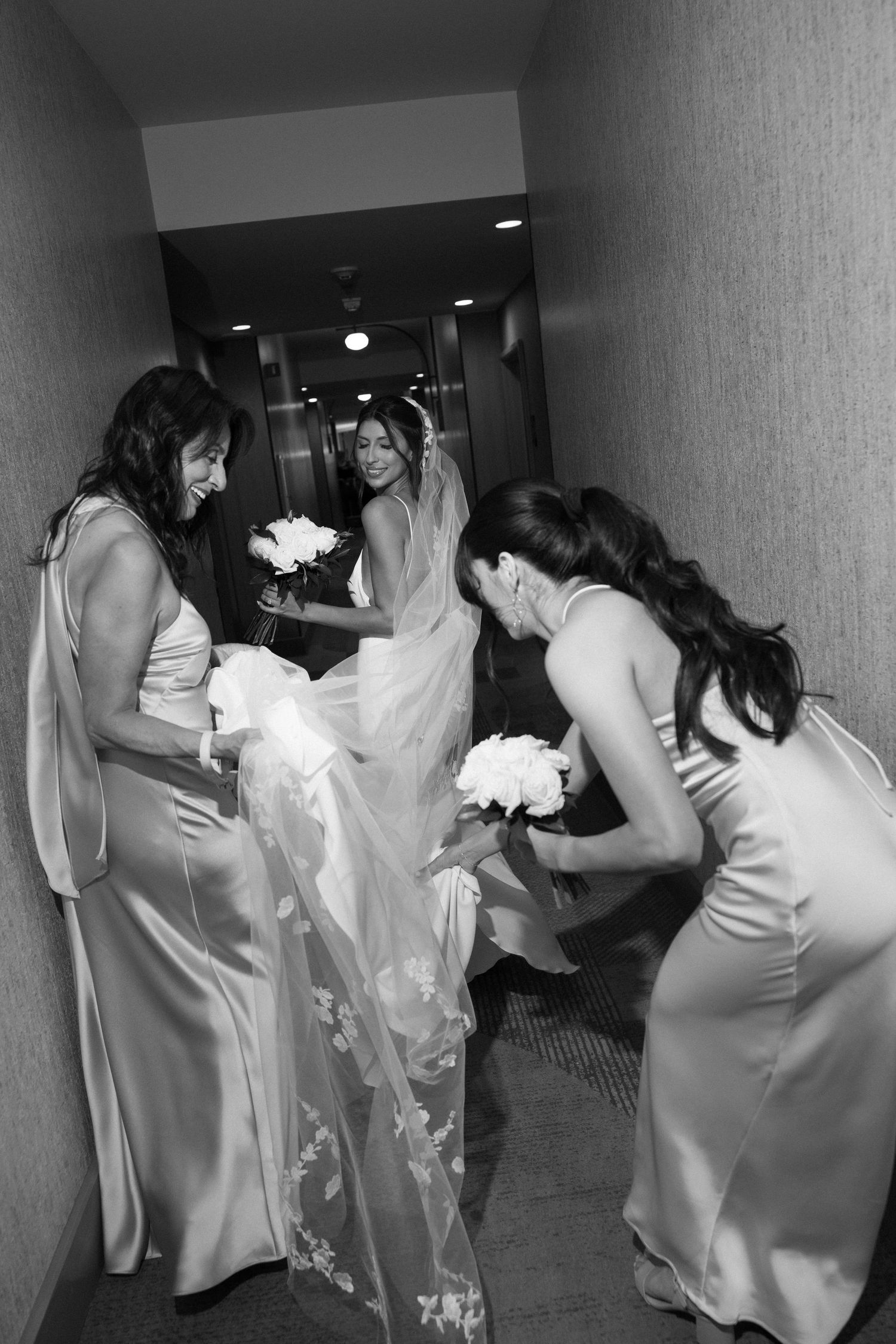 Wedding party in white dresses rushing through a hallway with excitement and movement.