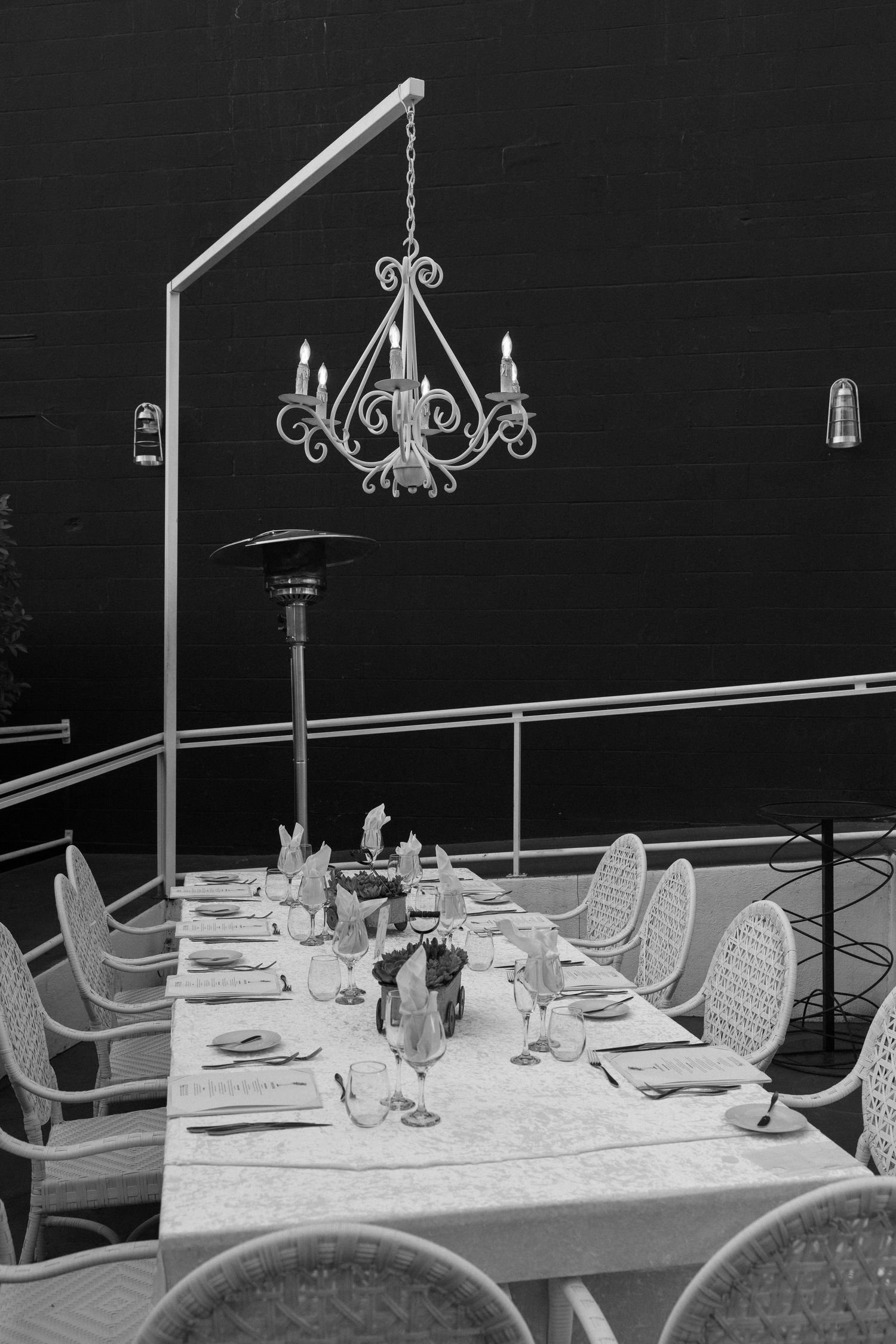 Black and white photo of an elegant outdoor dining table set for a formal dinner under a decorative chandelier.