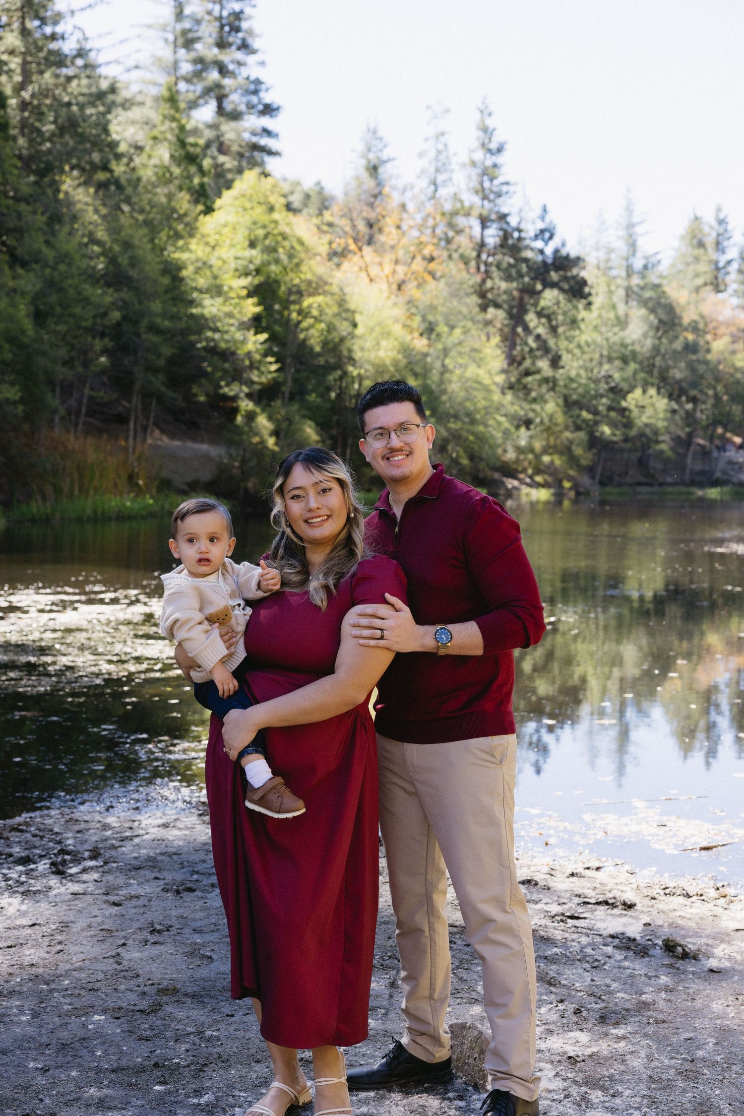 Family members in burgundy and khaki outfits sharing tender moments by a lake.