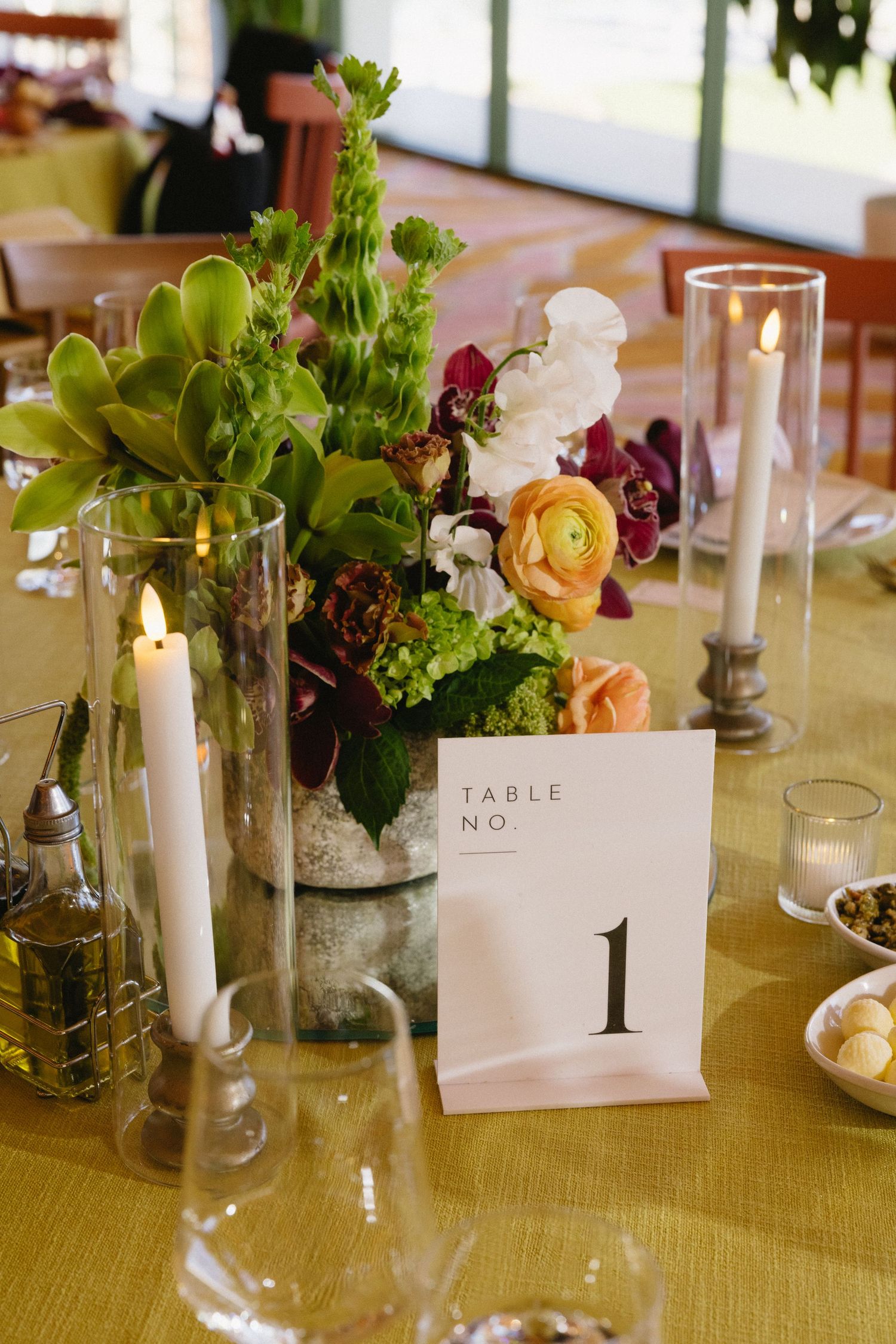 Elegant wedding Table No. 1 centerpiece with colorful flowers, succulents, and candles on a gold tablecloth.