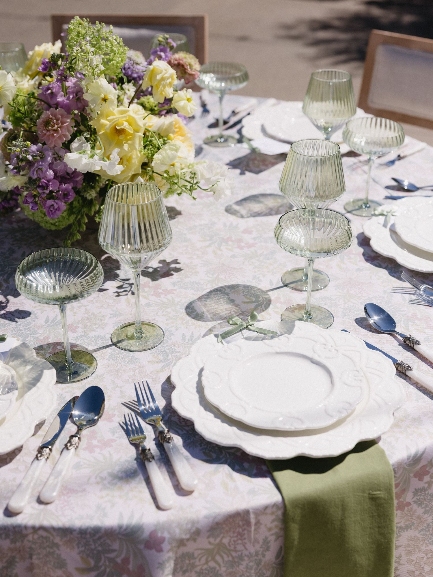 Elegant wedding tablescape with floral centerpiece, green glassware, white china, and sage linen napkins.