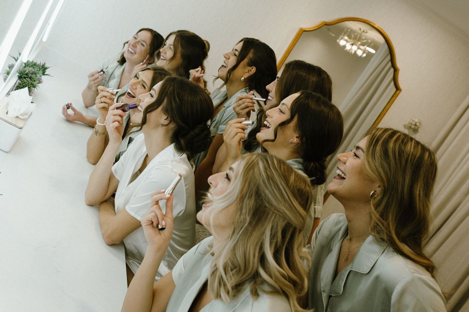 Group of bridesmaids laughing and holding heart props in front of a mirror during wedding preparations.