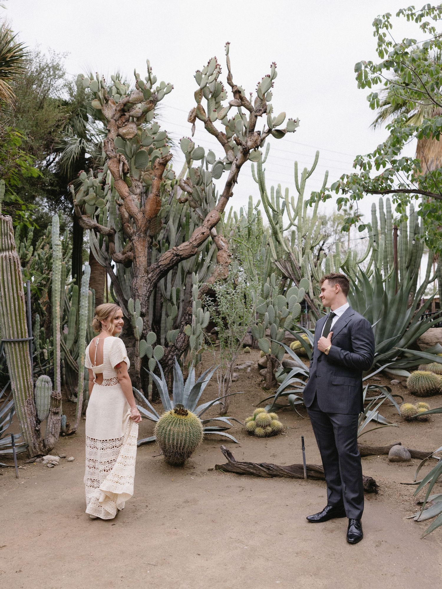 Bride and groom share a first look moment surrounded by towering cacti in a desert garden setting.