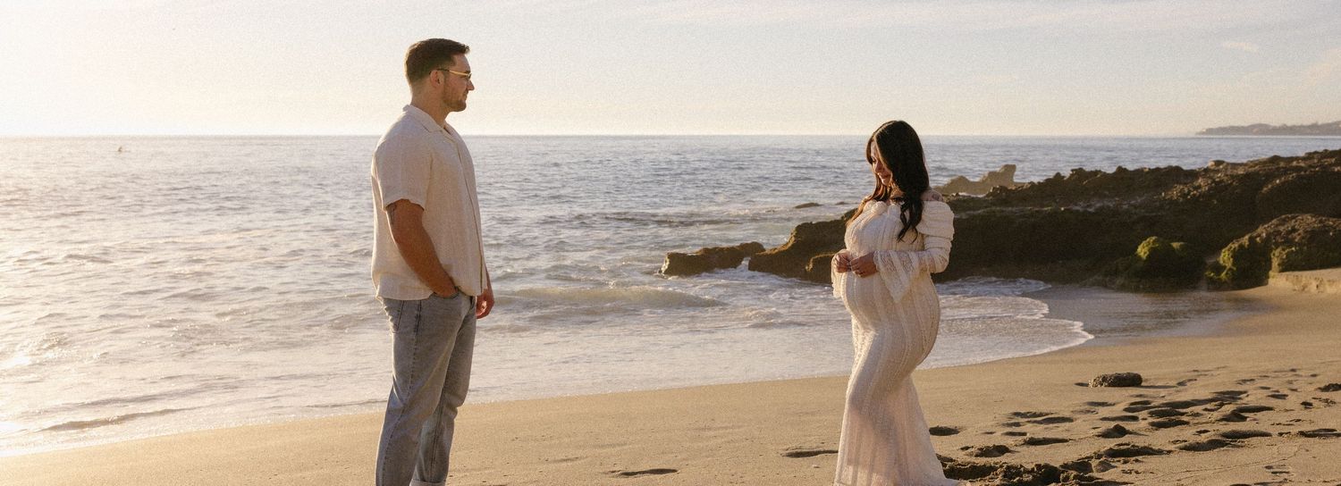 Couple walking along a scenic beach at sunset with waves crashing in the background.
