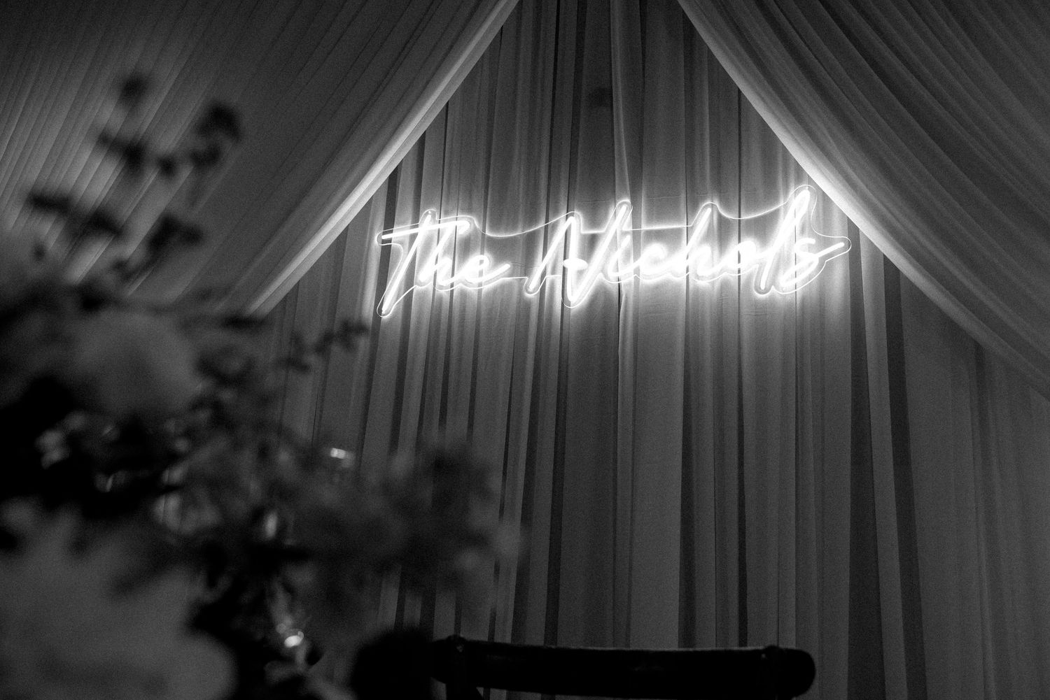 Black and white photo of a glowing neon sign reading The Atkins at a wedding reception.