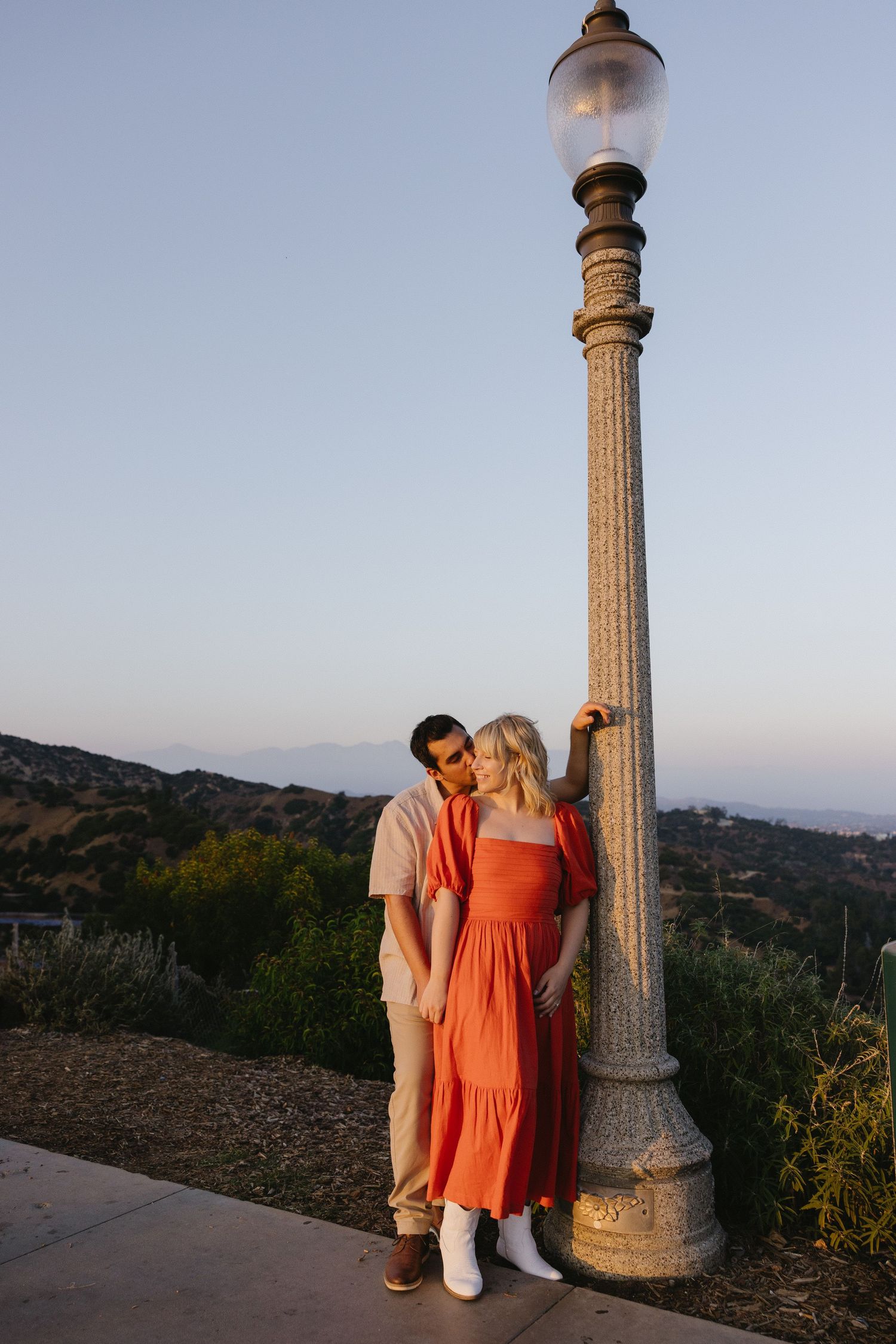 Couple posing near decorative stone pillars at Griffith Observatory during sunset.