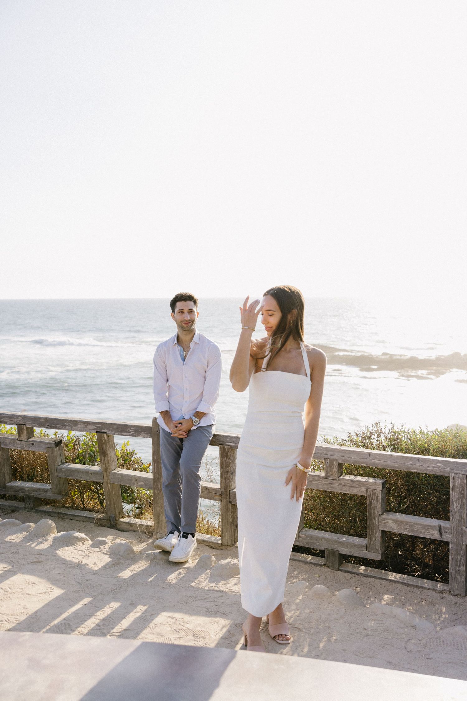 A couple in white attire sharing intimate moments by the ocean during sunset.