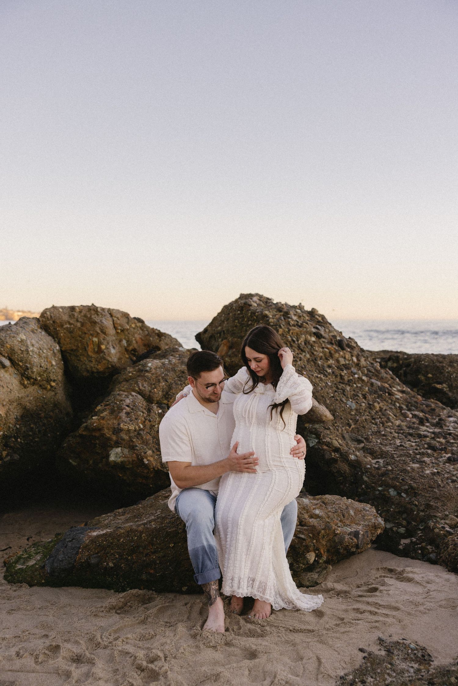A couple sits together on rocky coastal formations during golden hour.