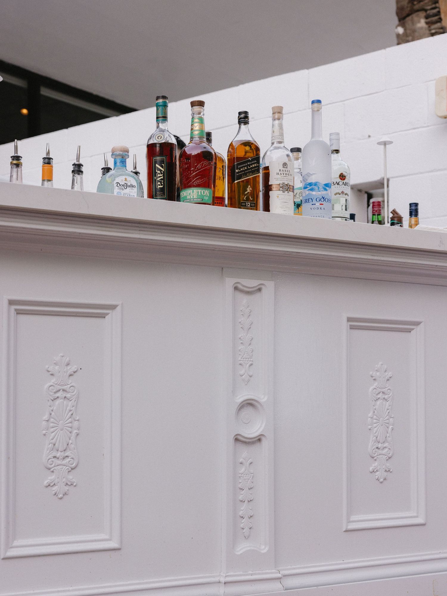 White ornate bar cabinet topped with assorted liquor bottles including whiskey, tequila, and vodka.