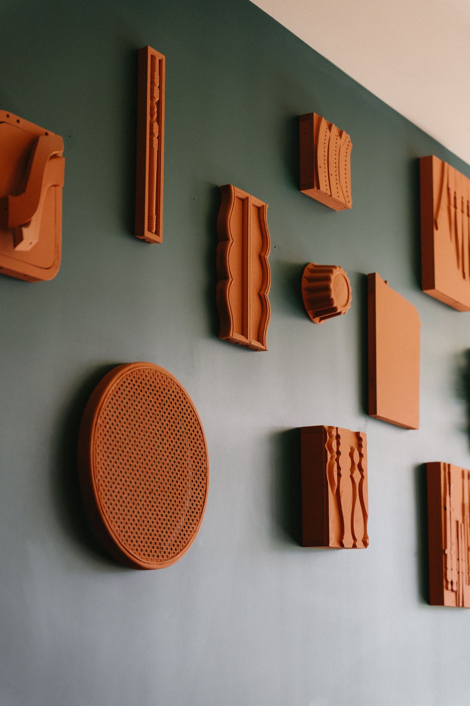 Terracotta ceramic wall art pieces in various geometric shapes displayed on a dark green wall.