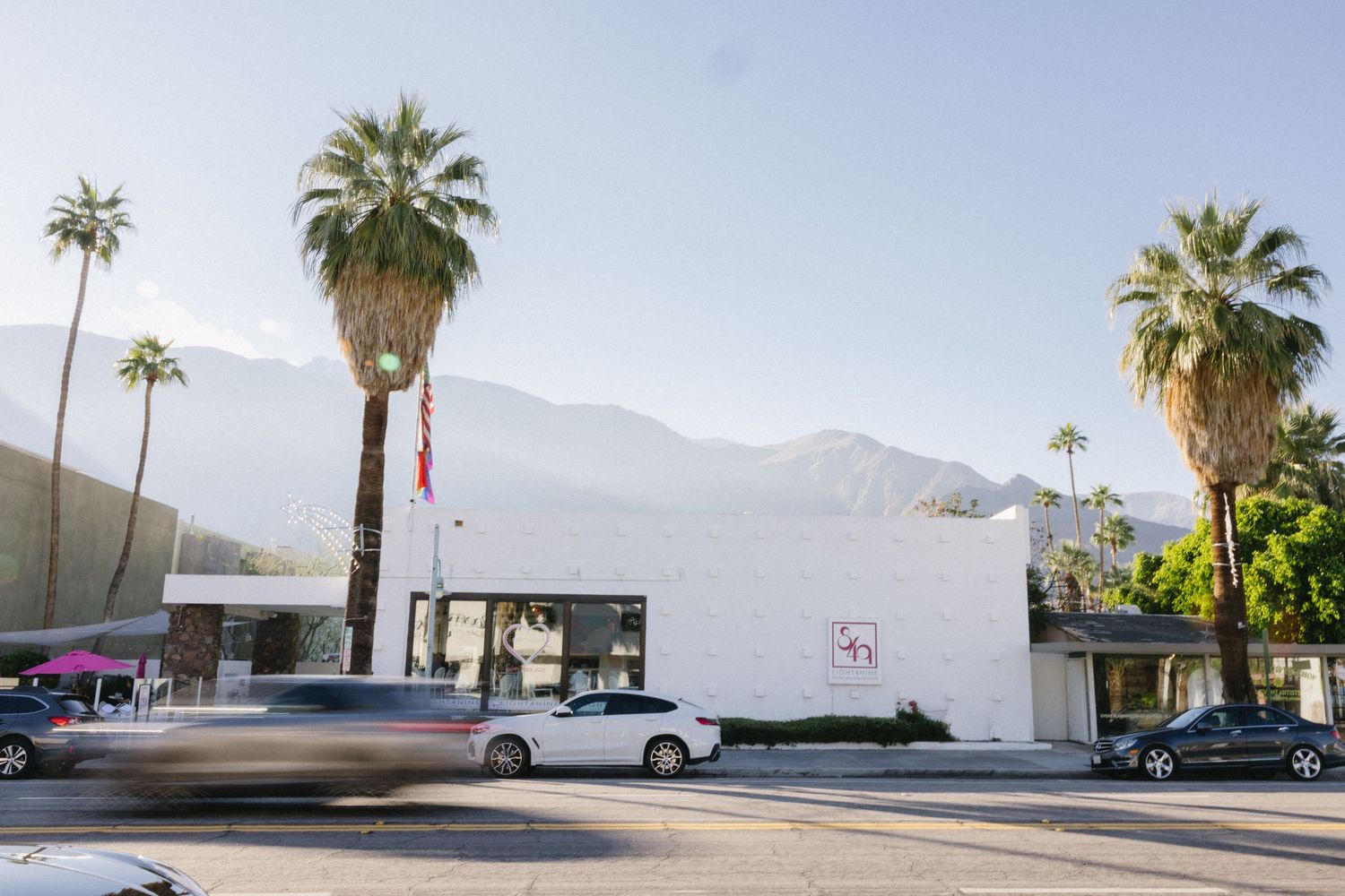 White modernist building with palm trees and mountain backdrop in Palm Springs, California.
