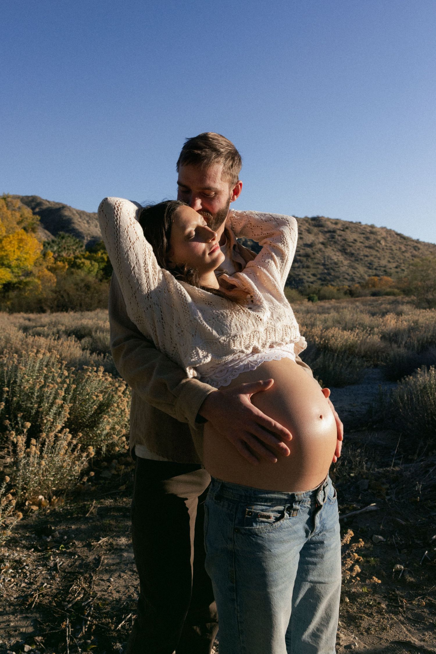 A couple embraces in a scenic mountain landscape with autumn foliage and desert brush.