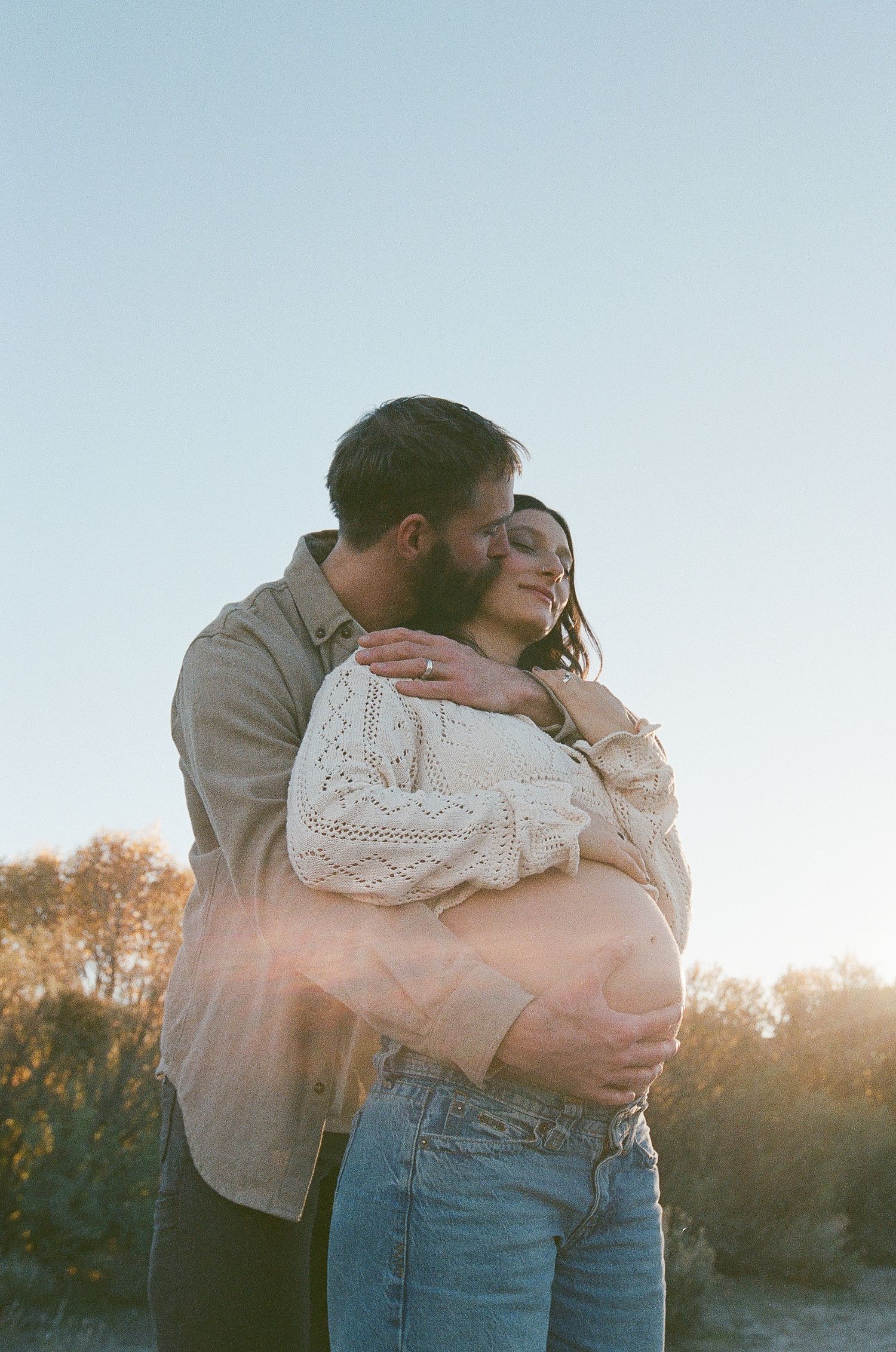 Tender embrace captured during golden hour with soft sky backdrop.