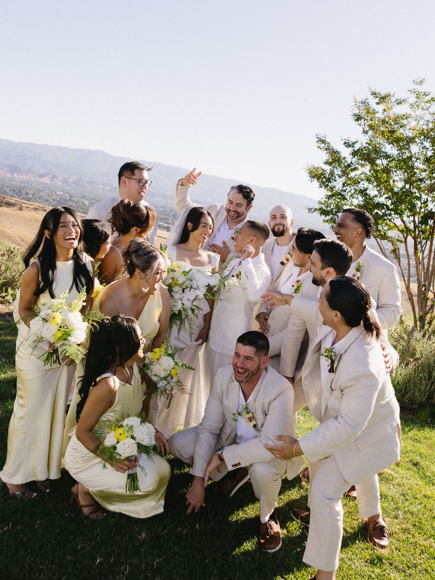 Wedding party in all-white attire laughing and celebrating outdoors.