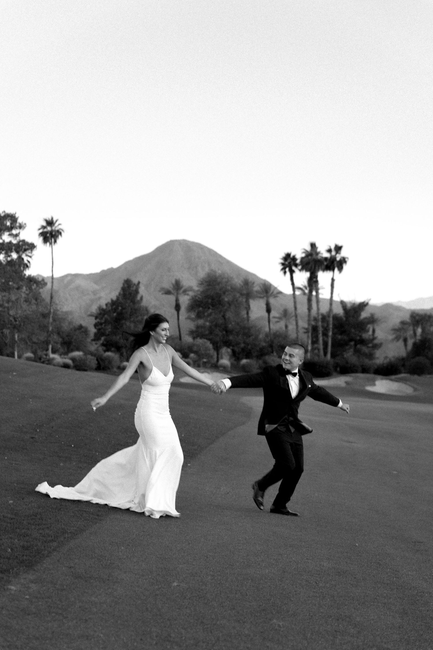 Playful black and white sequence of couple dancing on grass with mountains in background.