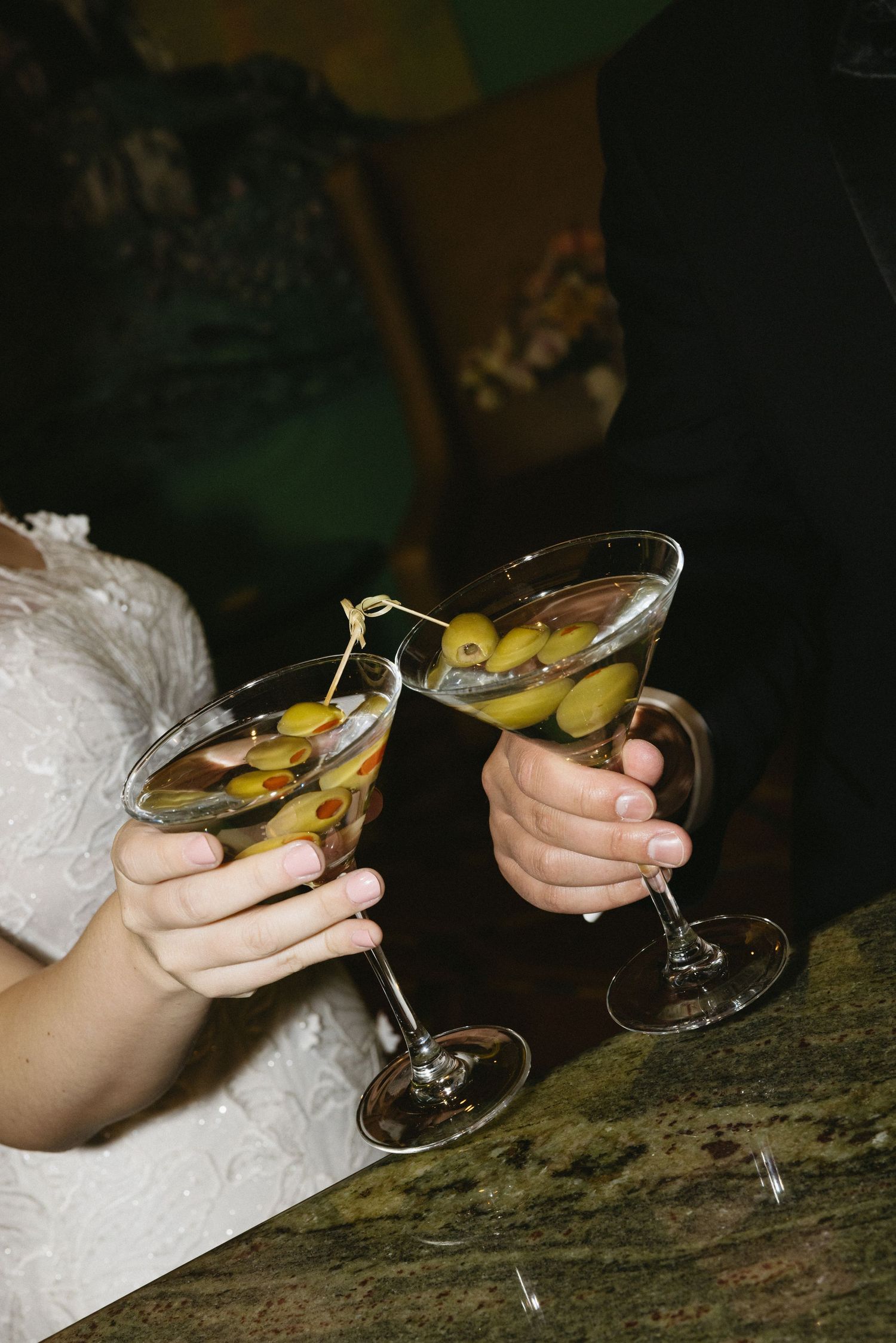 Bride and groom clinking martini glasses with olives at wedding reception.