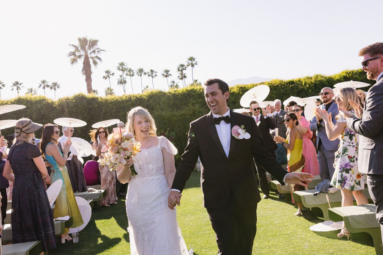 Bride and groom walk down the aisle at an outdoor Palm Springs wedding ceremony with guests cheering.